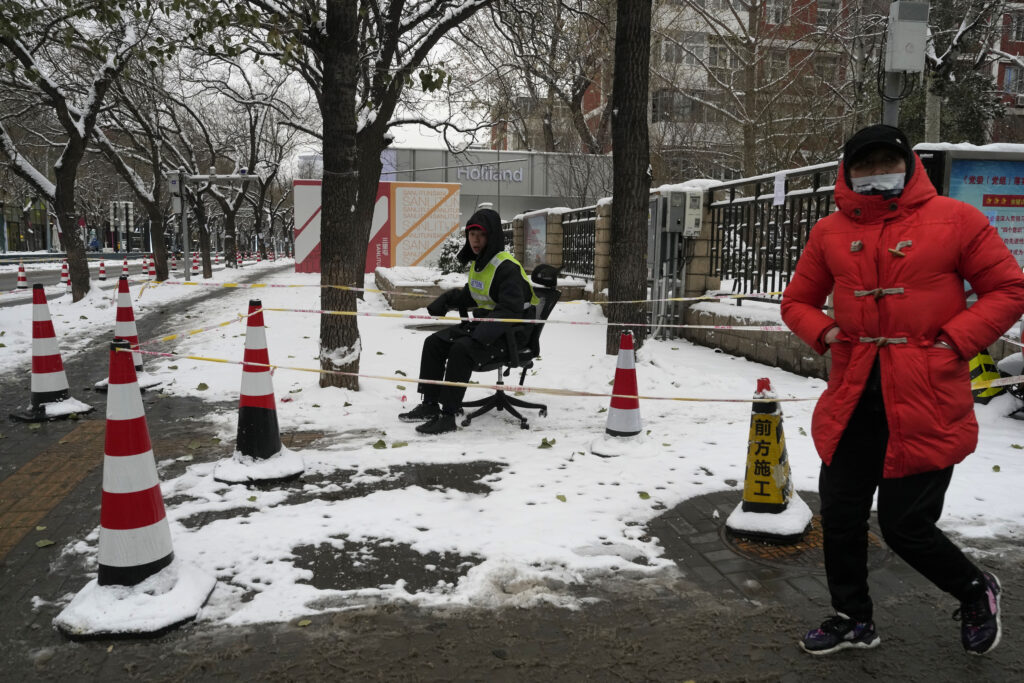 A security guard sits on an office card to guard an area cordoned off to stop people parking their bicycles in Beijing, Thursday, Dec. 14, 2023. Snow fall in the Chinese capital this week is expected to be followed by bitter (AP Photo/Ng Han Guan)