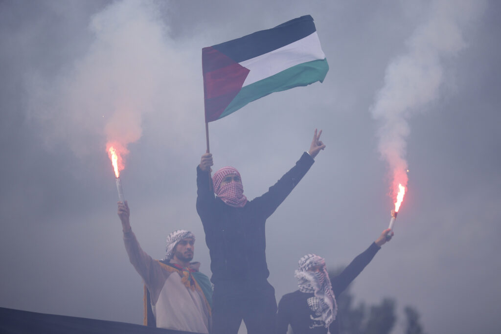 A Bosnian Muslim man waves a Palestinian flag backdroped by burning torches during a protest against Israel and in support of Palestinians in Sarajevo, Bosnia, Sunday, Oct. 22, 2023. (AP Photo/Armin Durgut)