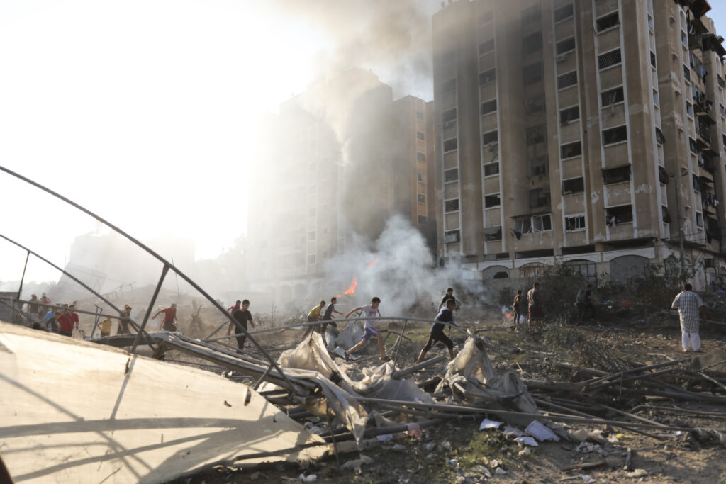 Palestinians run by the building destroyed in an Israeli airstrike on Nusseirat refugee camp, Gaza Strip, Wednesday, Oct. 18, 2023. (AP Photo/Ali Mohmoud)