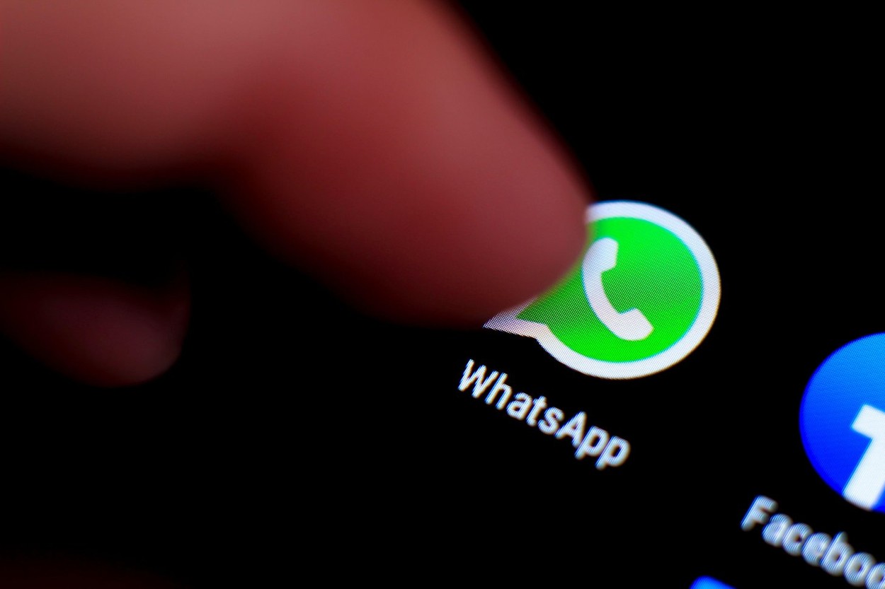 Madrid, Spain- March 3, 2021: Finger pressing Whatsapp icon on black mobile phone screen. Facebook icon in the background.