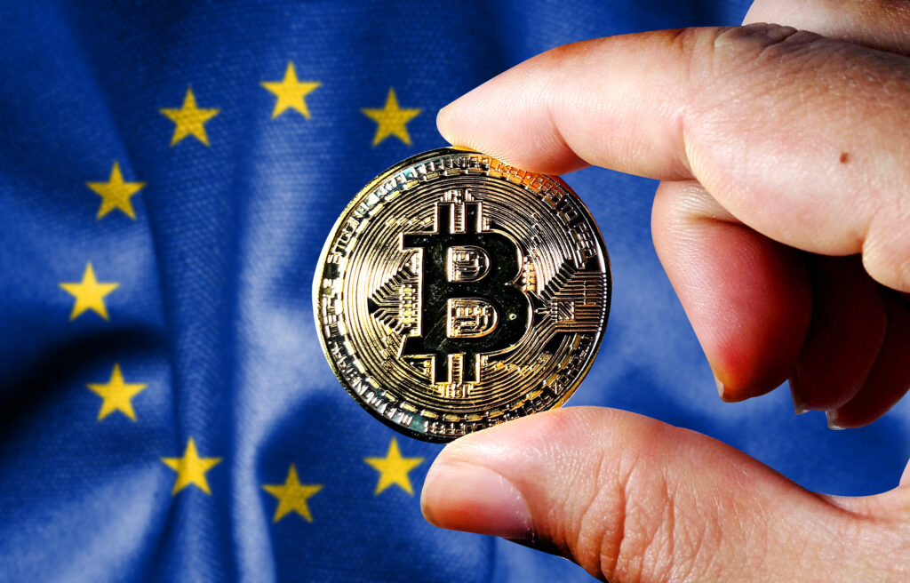Hold the physical version of Bitcoin (the new virtual currency) and the European Union flag. EU cryptocurrency and blockchain technology investor concept map (the background is deliberately blurred)