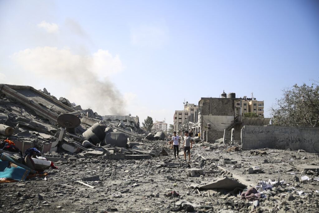 Palestinians boys walk by the buildings destroyed in the Israeli bombardment on al-Zahra, on the outskirts of Gaza City, Friday, Oct. 20, 2023. (AP Photo/Ali Mahmoud)
