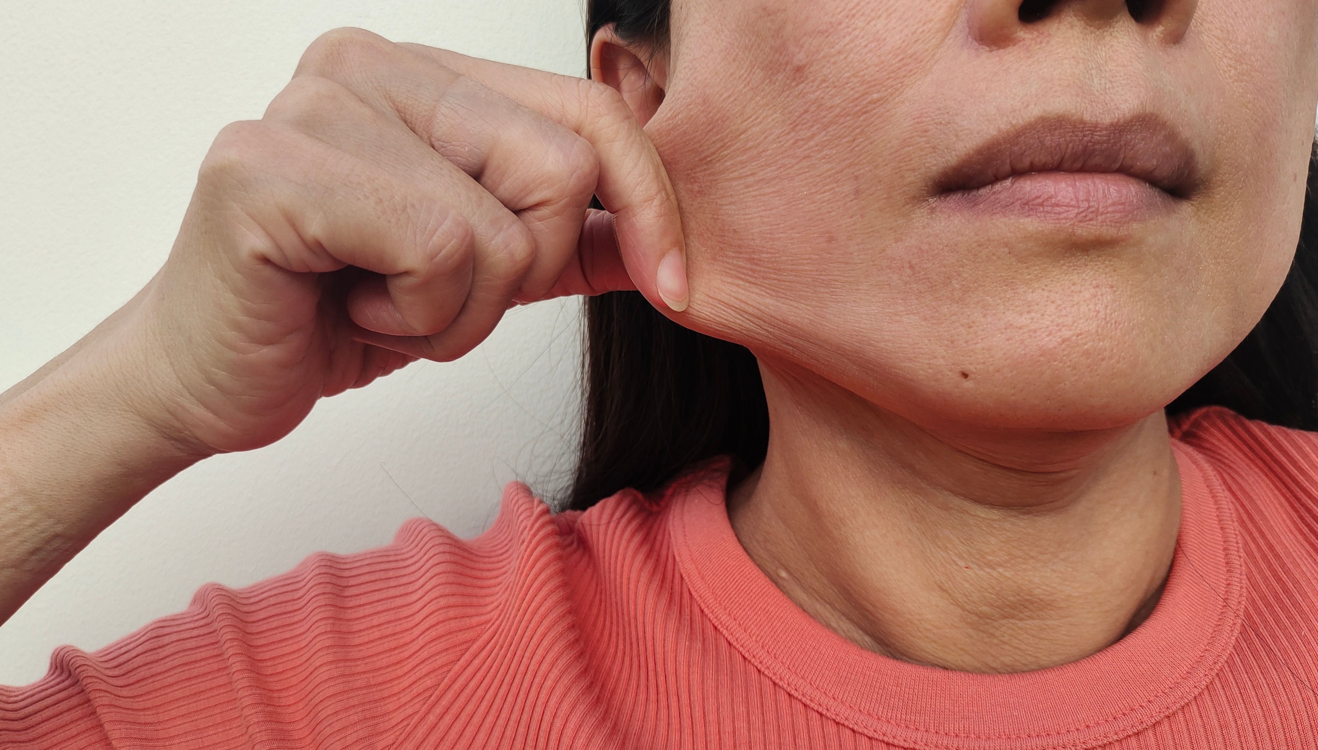 portrait showing the fingers squeezing the flabbiness adipose hanging skin beside the face, problem wrinkle and flabby skin on the face, dark spots on face of the woman, concept health care.