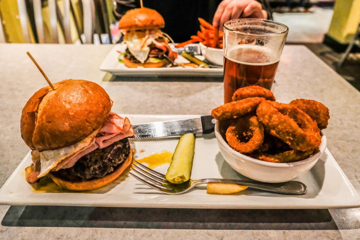 A Close up View of a Big Burger, Fried Onion Rings, and a Cold Beer