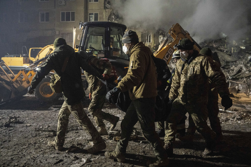 Ukrainian servicemen carry a body of a man who was killed by a Russian rocket attack at residential neighborhood in the southeastern city of Dnipro, Ukraine, Saturday, Jan. 14, 2023. (AP Photo/Evgeniy Maloletka)