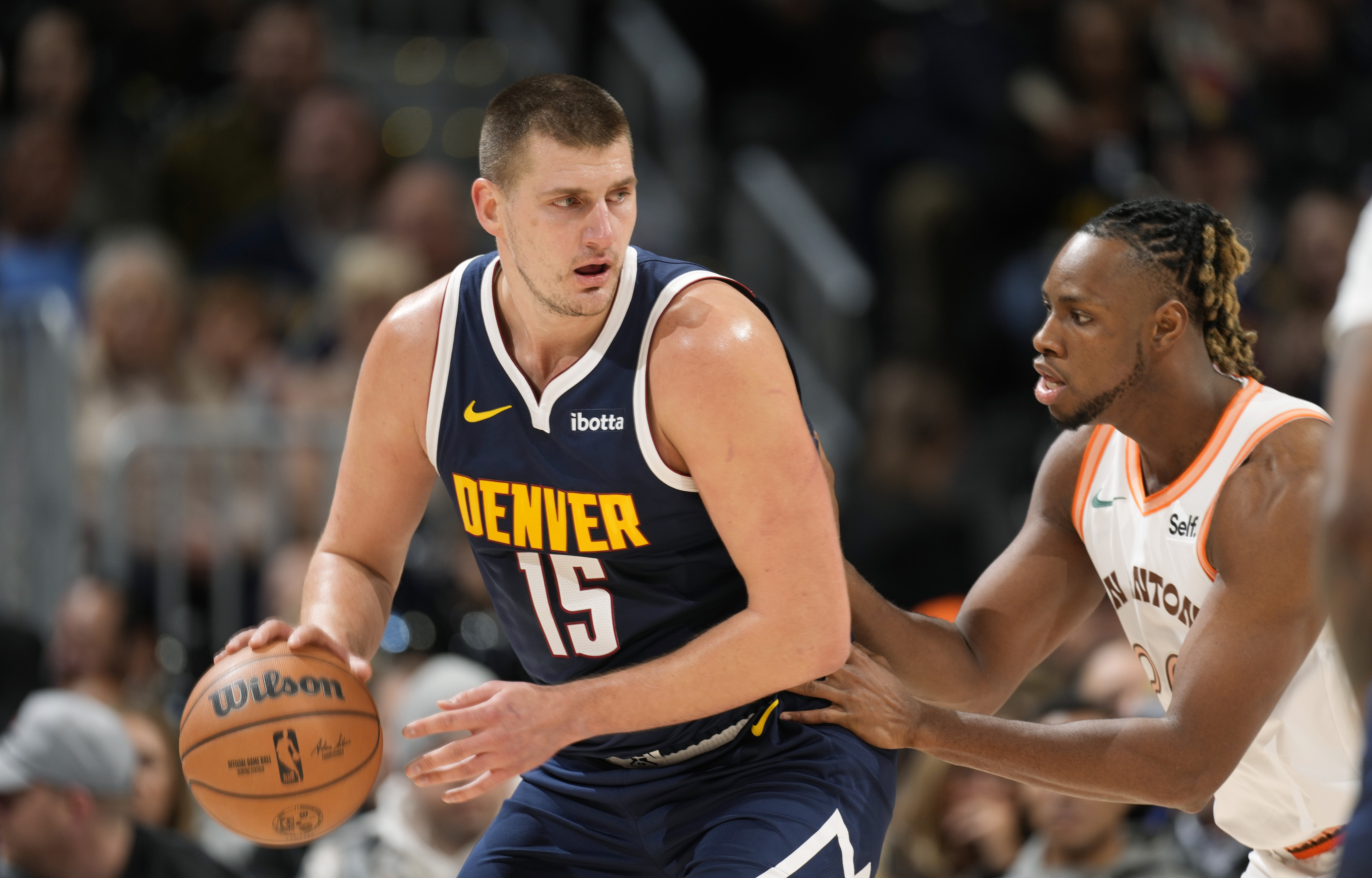 Denver Nuggets center Nikola Jokic, left, looks to drive to the basket as San Antonio Spurs center Charles Bassey, right, defends in the first half of an NBA basketball game on Sunday, Nov. 26, 2023, in Denver. (AP Photo/David Zalubowski)