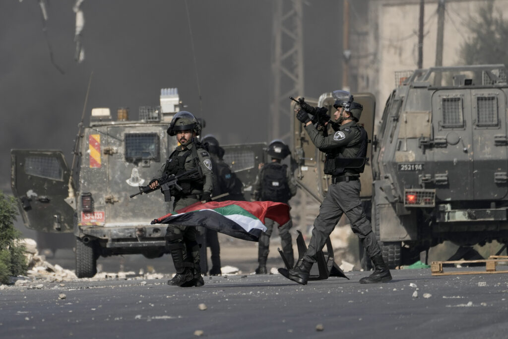 Israeli bored policeman holds a Palestinian flag he took from Palestinians during clashes following a demonstration in support of the Gaza Strip in the West Bank city of Nablus, Friday, Oct. 13, 2023. (AP Photo/Majdi Mohammed)