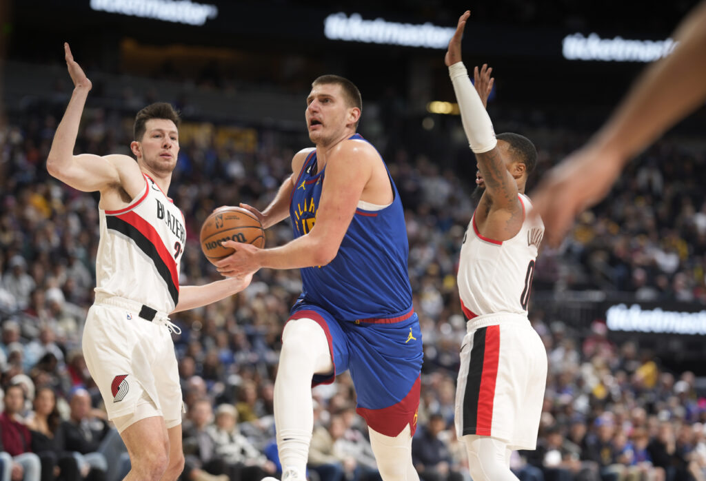 Denver Nuggets center Nikola Jokic, center, drives to the basket between Portland Trail Blazers forward Drew Eubanks, left, and guard Damian Lillard in the second half of an NBA basketball game Friday, Dec. 23, 2022, in Denver. (AP Photo/David Zalubowski)