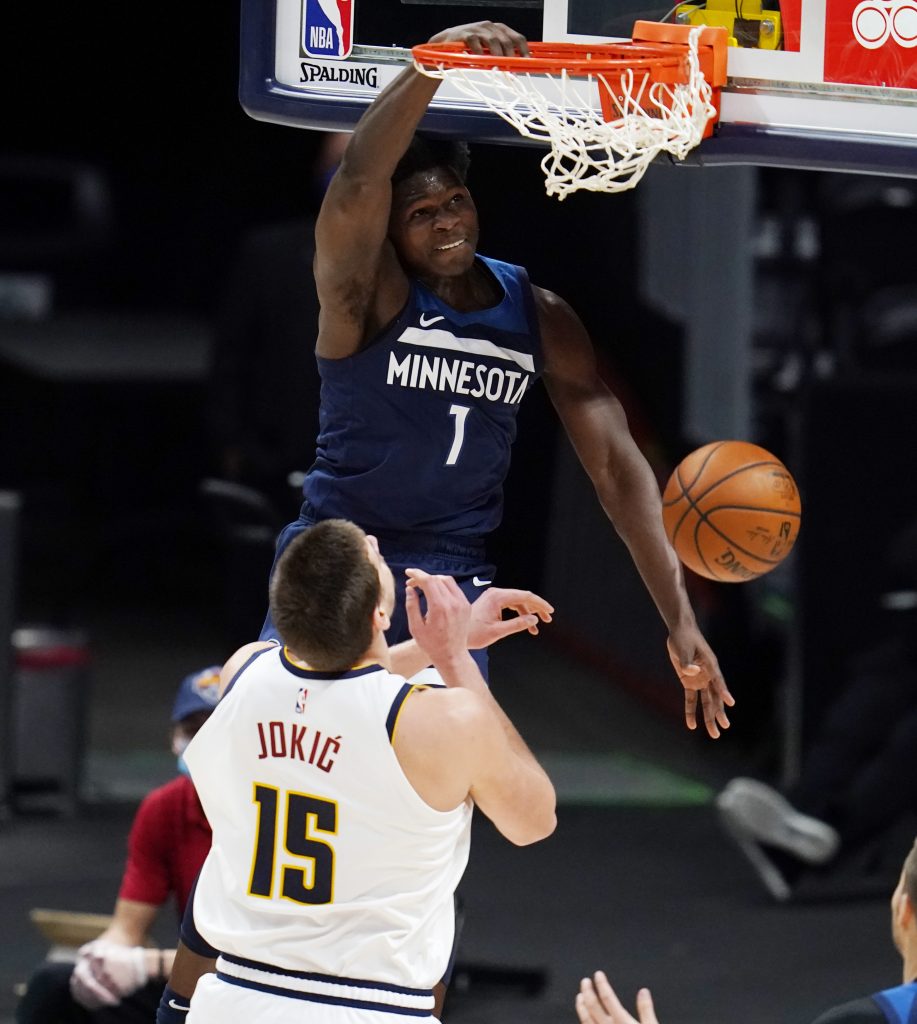 Minnesota Timberwolves guard Anthony Edwards (1) hangs from the rim after dunking the ball for a basket over Denver Nuggets center Nikola Jokic (15) in the first half of an NBA basketball game Tuesday, Jan.5, 2021, in Denver. (AP Photo/David Zalubowski)