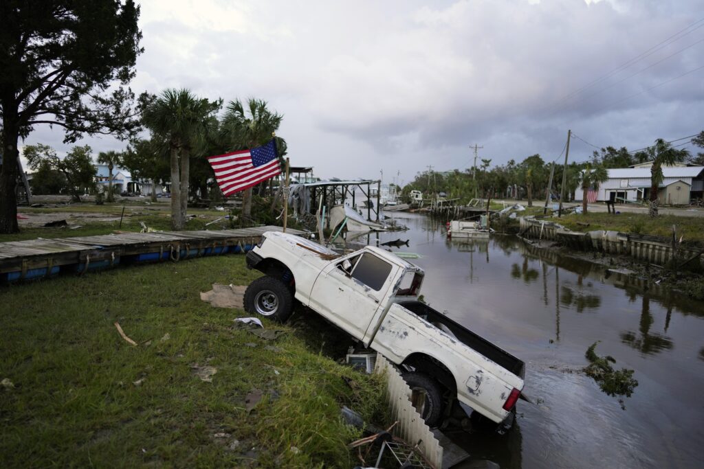 A pickup truck with an American flag tied to sits halfway into a canal in Horseshoe Beach, Fla., after the passage of Hurricane Idalia, Wednesday, Aug. 30, 2023. (AP Photo/Rebecca Blackwell)
