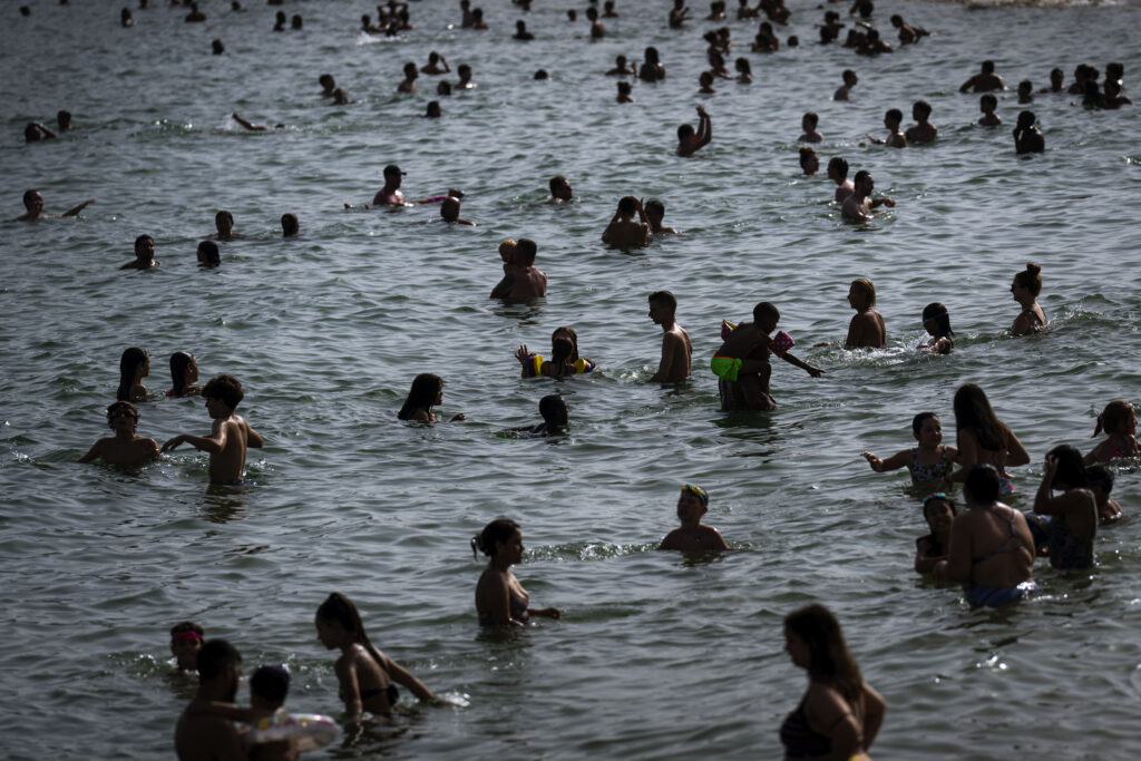 People cool off on a beach in Barcelona, Spain, Wednesday, July 12, 2023. More than 10 of Spain's regions are on red alert for the second day of the latest heat wave, with temperatures topping 40 degrees Celsius. (AP Photo/Emilio Morenatti)