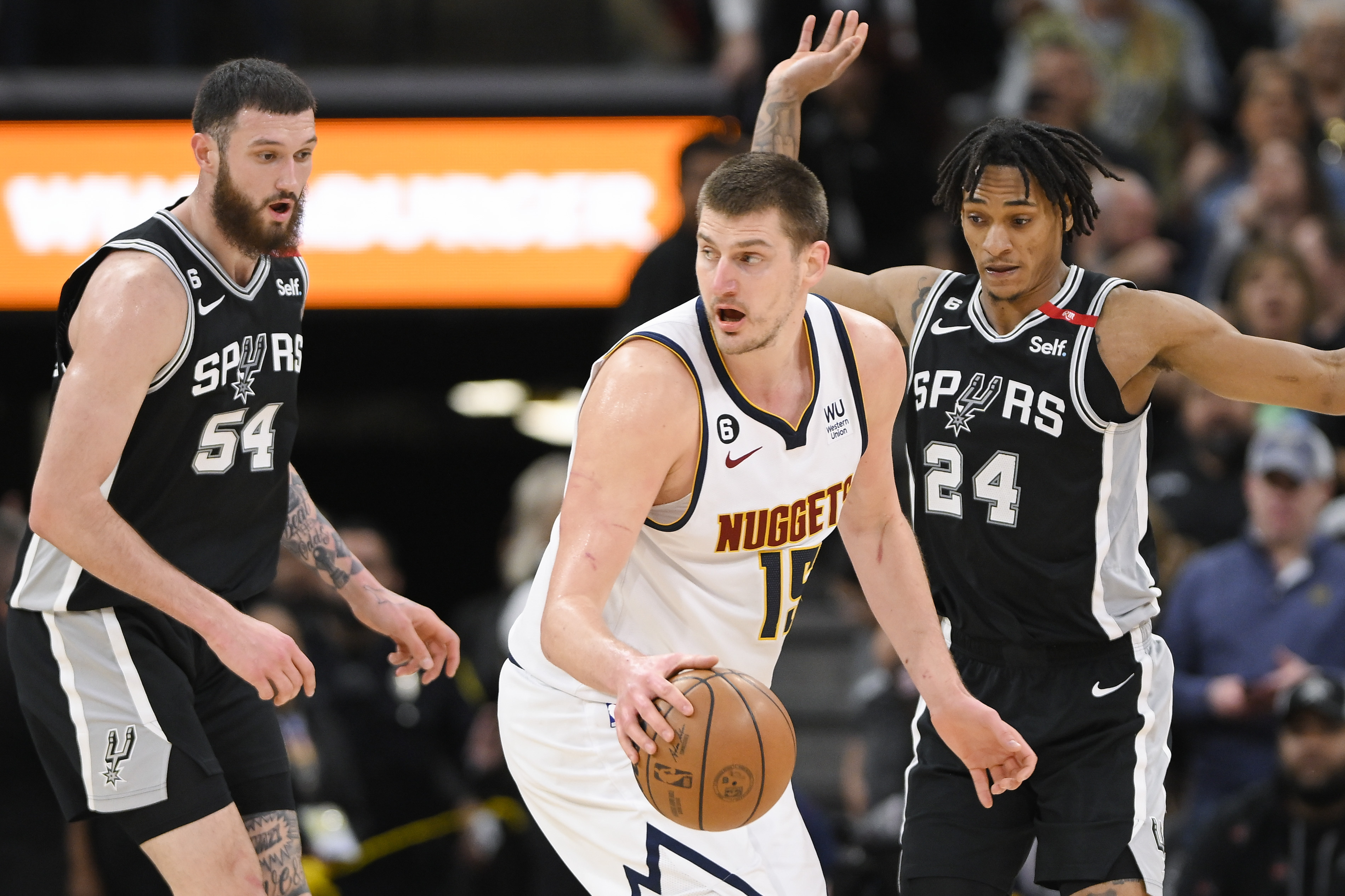Denver Nuggets' Nikola Jokic, center, drives against San Antonio Spurs' Sandro Mamukelashvili (54) and Devin Vassell during the second half of an NBA basketball game, Friday, March 10, 2023, in San Antonio. (AP Photo/Darren Abate)