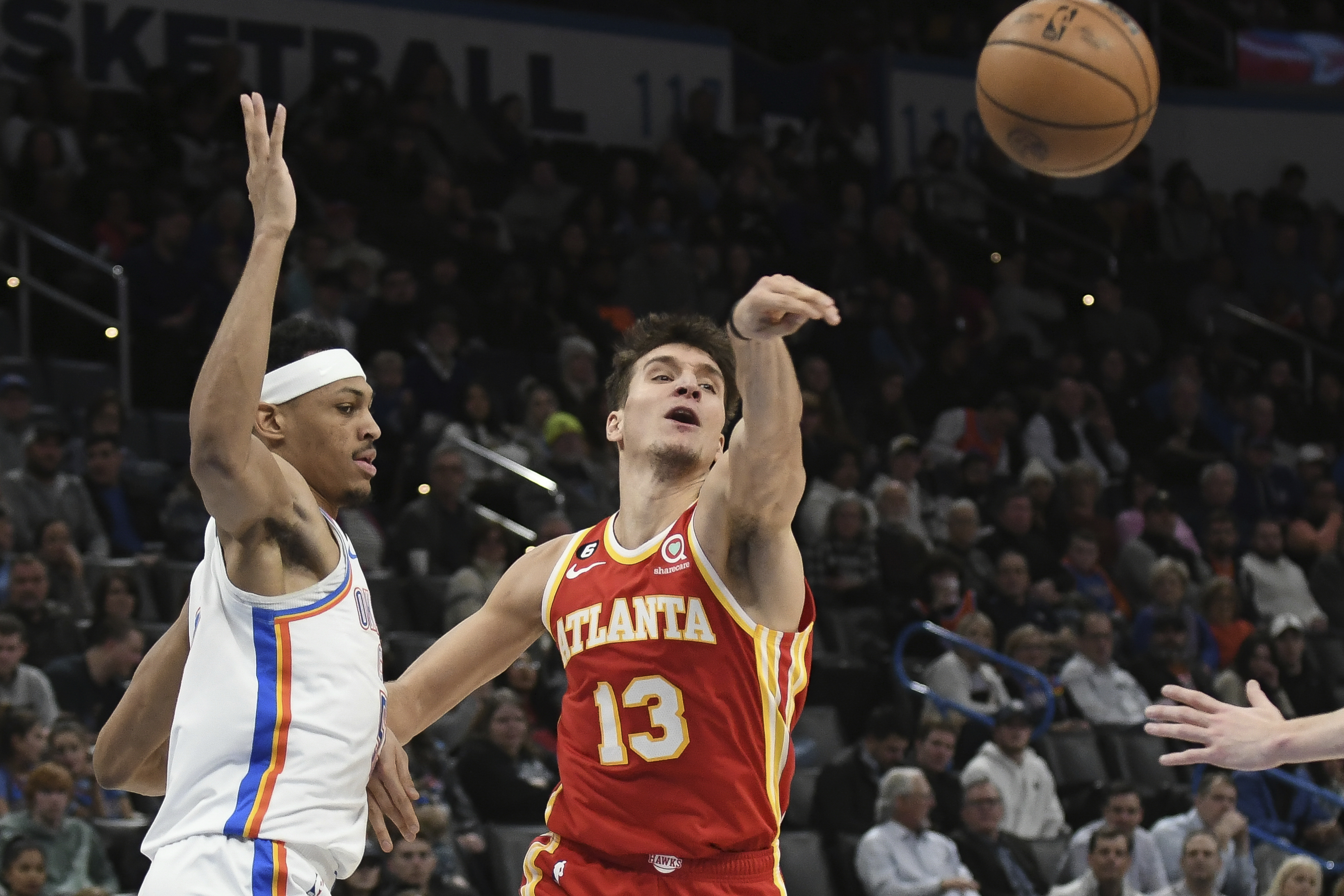 Atlanta Hawks forward Bogdan Bogdanovic, right, passes the ball past Oklahoma City Thunder forward Darius Bazley, left, in the first half of an NBA basketball game, Wednesday, Jan. 25, 2023, in Oklahoma City. (AP Photo/Kyle Phillips)