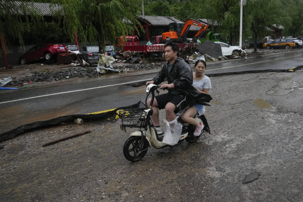 People ride past damaged road and vehicles swept by floodwaters in the Mentougou district as continuous rain fall triggers alerts in Beijing, Monday, July 31, 2023. (AP Photo/Andy Wong)