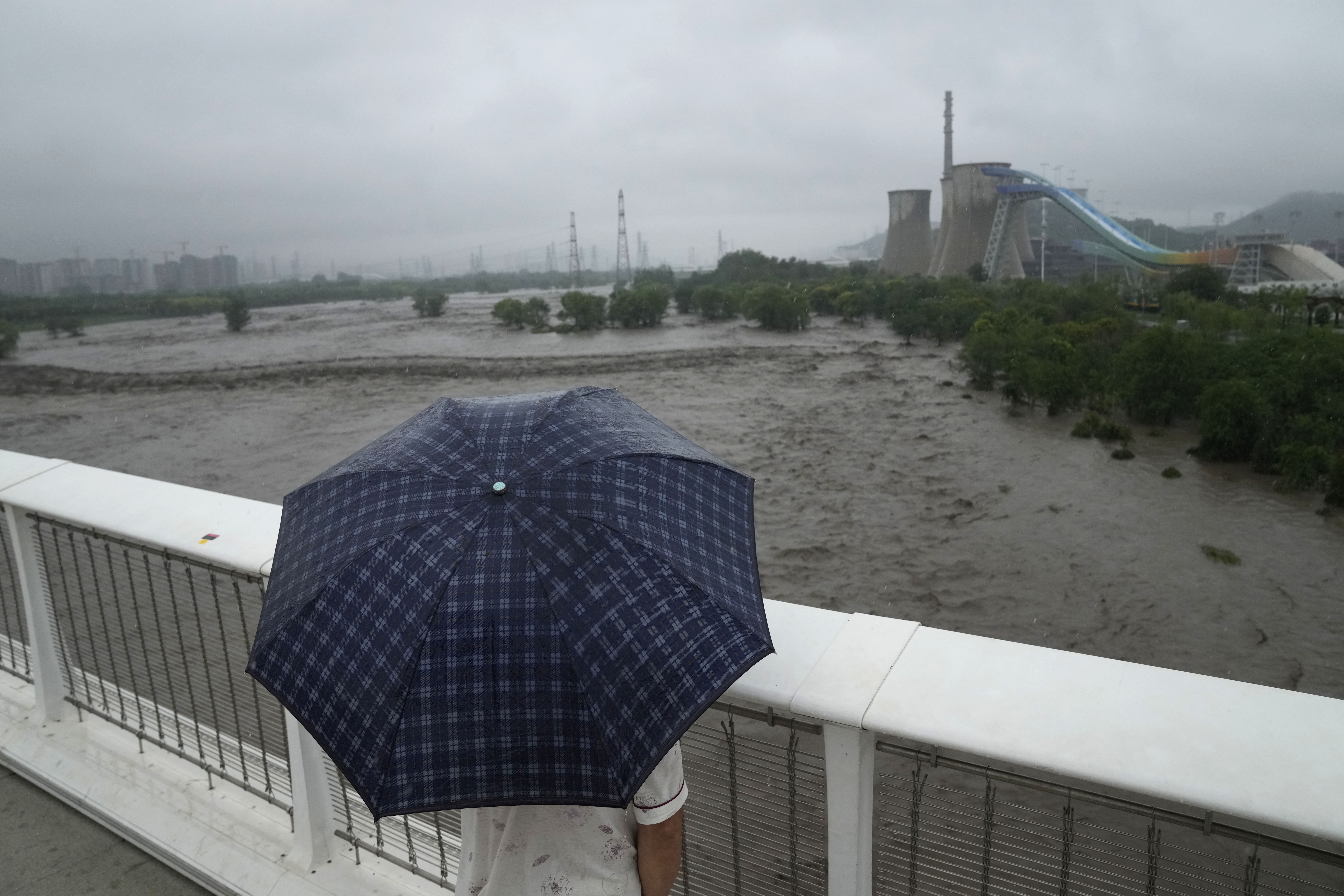 A man holding an umbrella looks out from a bridge over a swollen Yongding river near the Shougang park as continuous rain fall triggers alerts in Beijing, Monday, July 31, 2023. (AP Photo/Andy Wong)