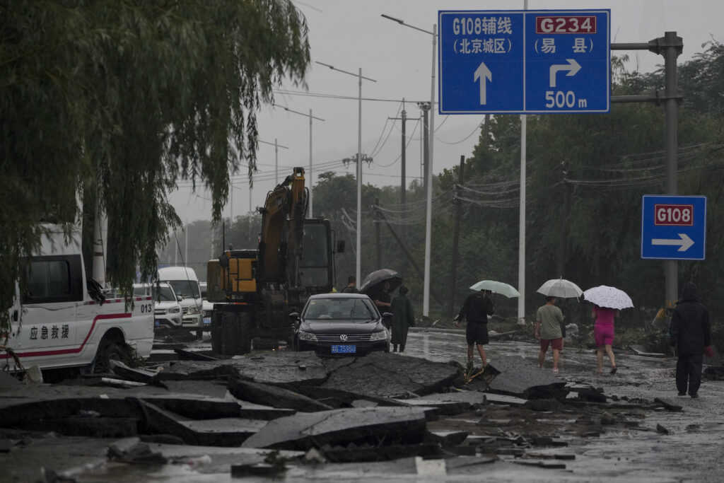 People and vehicles pass through a road damaged by floodwaters in the Mentougou district as continuous rainfall triggers alerts in Beijing, Monday, July 31, 2023. (AP Photo/Andy Wong)