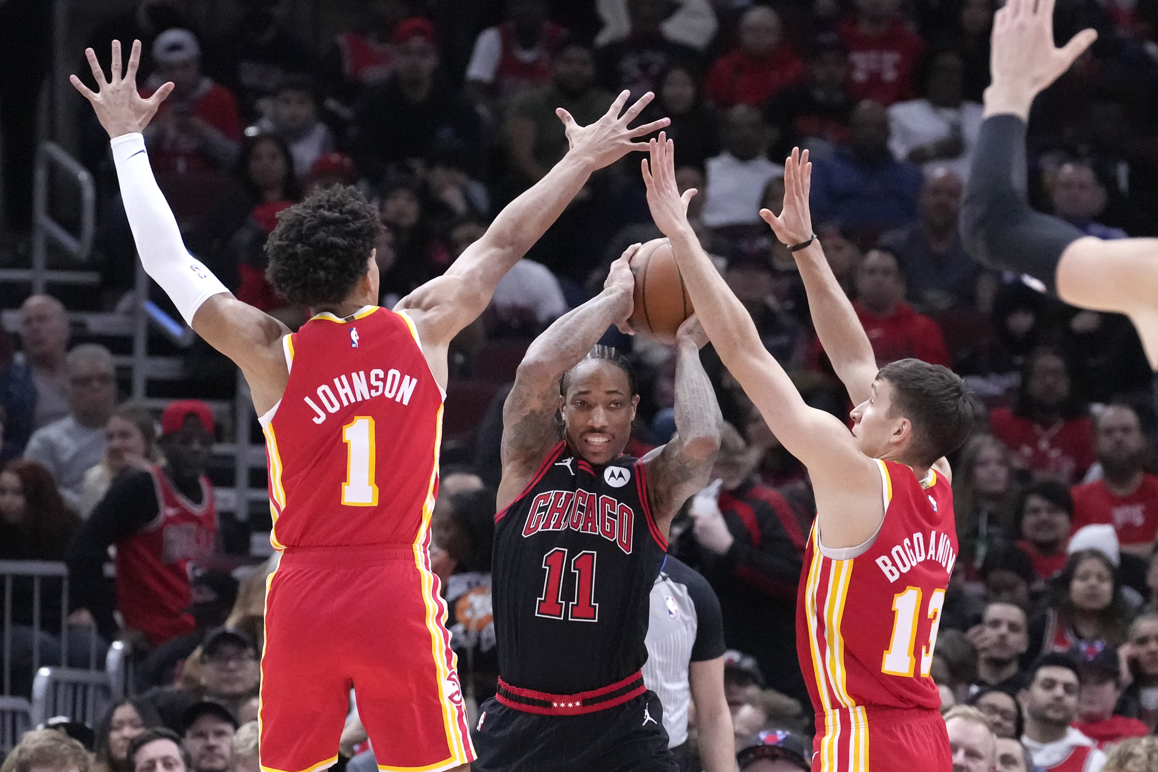 Chicago Bulls' DeMar DeRozan (11) looks to pass under pressure from Atlanta Hawks' Jalen Johnson (1) and Bogdan Bogdanovic during the first half of an NBA basketball game Monday, Jan. 23, 2023, in Chicago. (AP Photo/Charles Rex Arbogast)