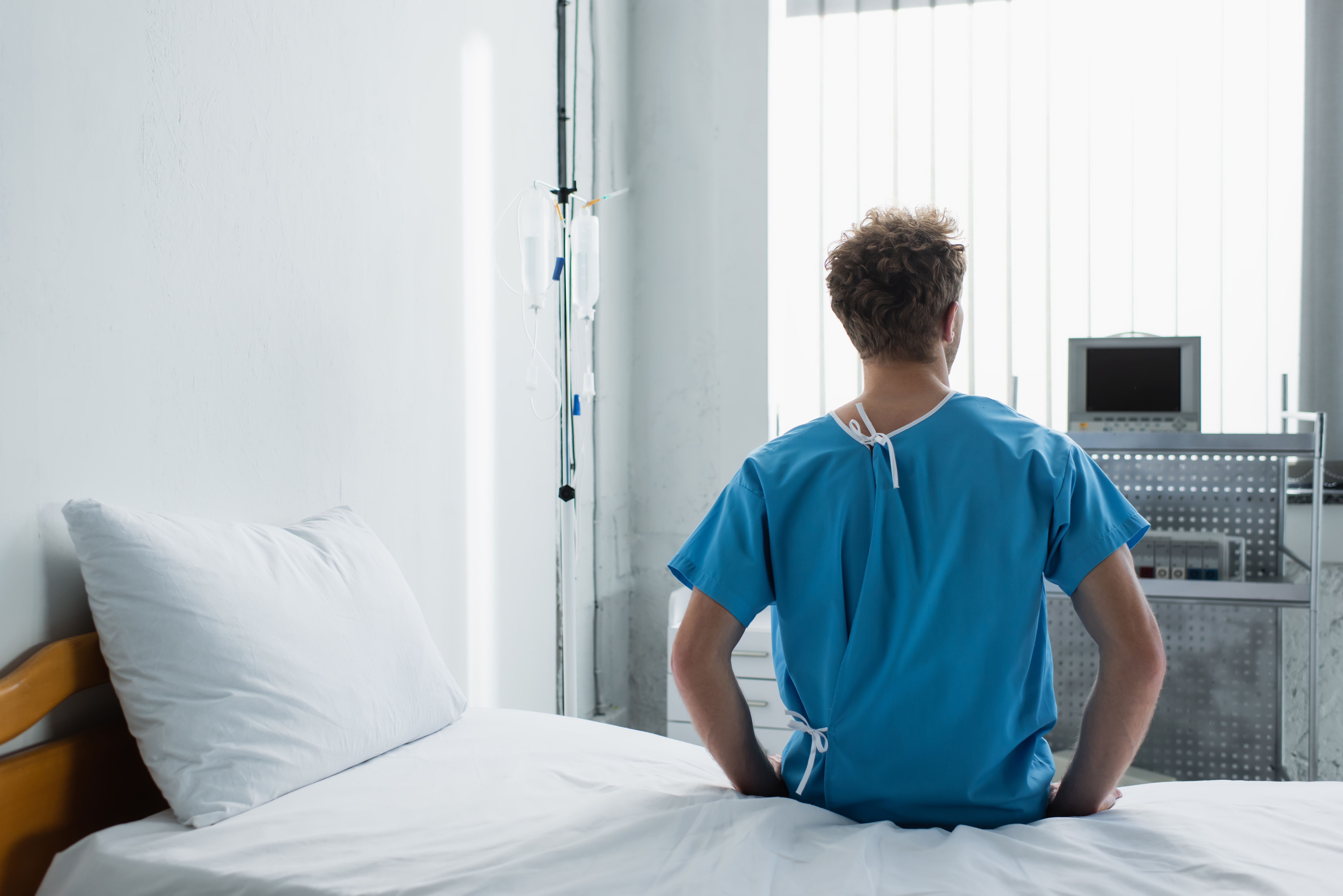 Back,View,Of,Curly,Man,Sitting,On,Hospital,Bed
