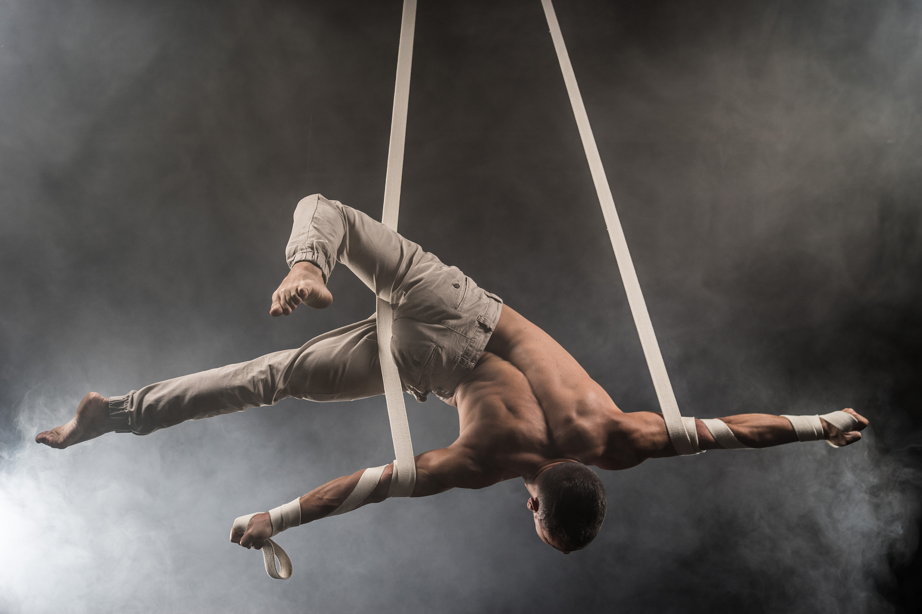 circus artist on the aerial straps with Strong muscles on the background of smoke