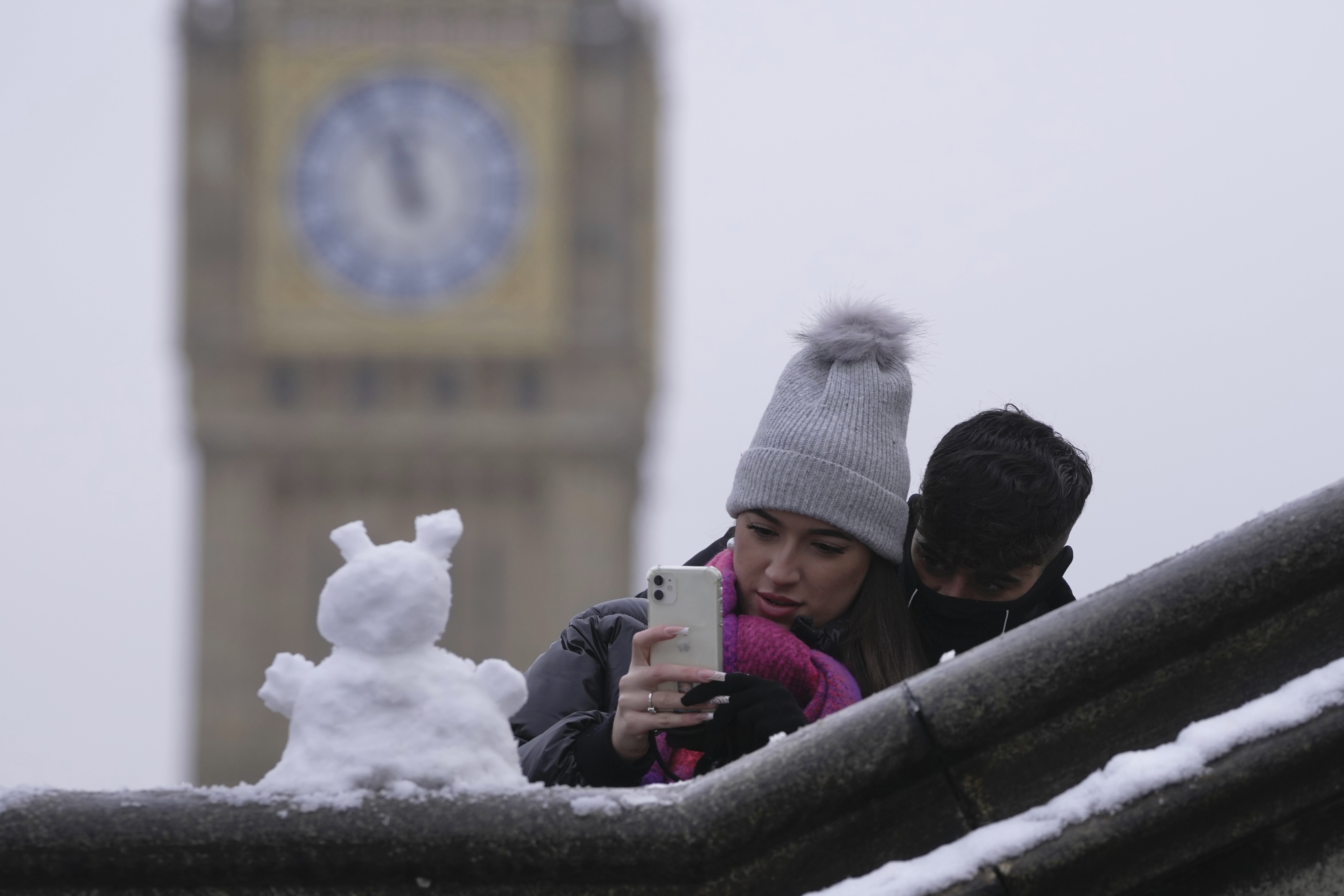 A couple take photo of a snowman in London, Monday, Dec. 12, 2022. Snow and ice have swept across parts of the UK, with cold wintry conditions set to continue for days. (AP Photo/Kin Cheung)
