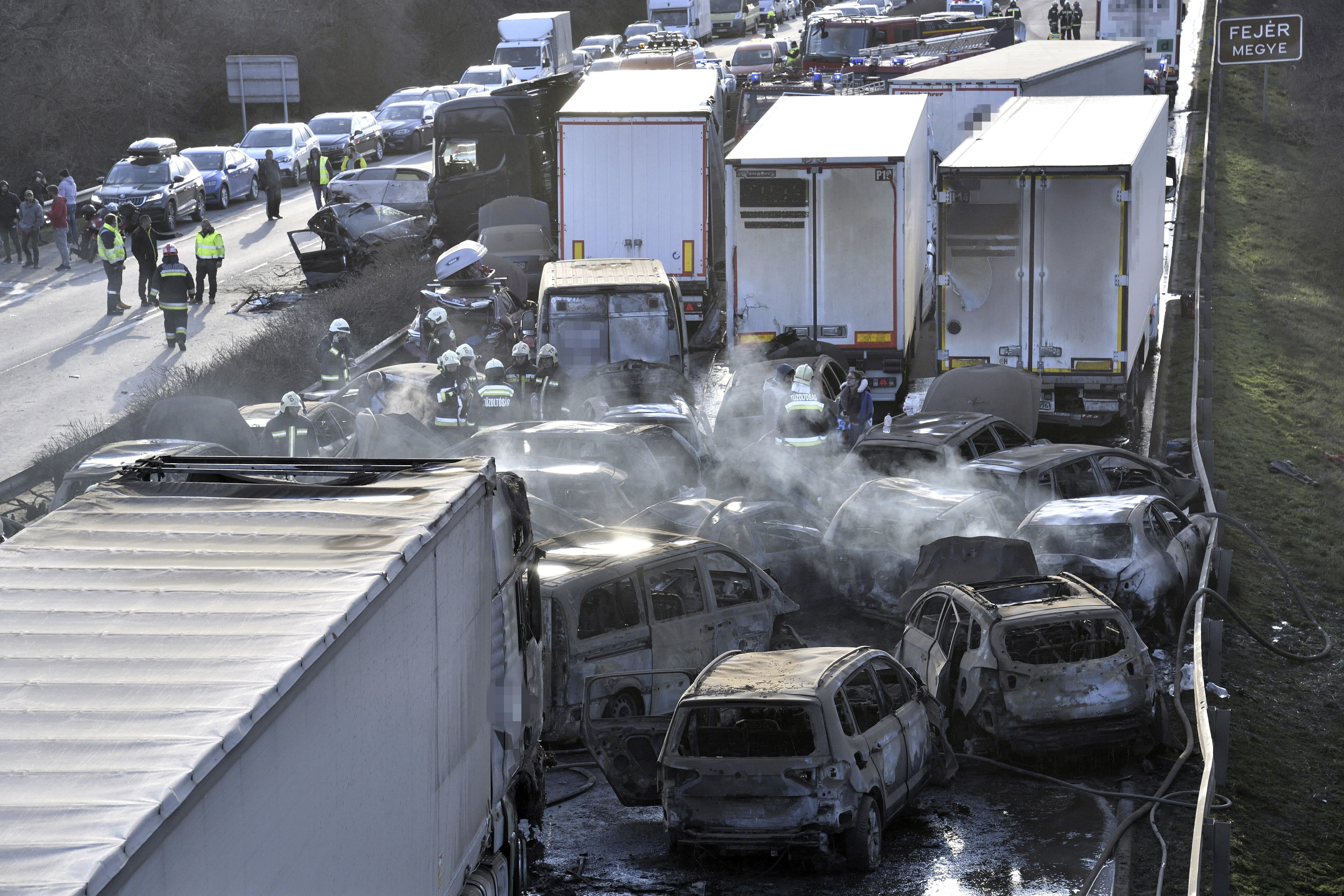 Firefighters work among smouldering cars after several trucks and cars crashed on M1 motorway near Herceghalom, Hungary, Saturday, March 11, 2023. (Peter Lakatos/MTI via AP)