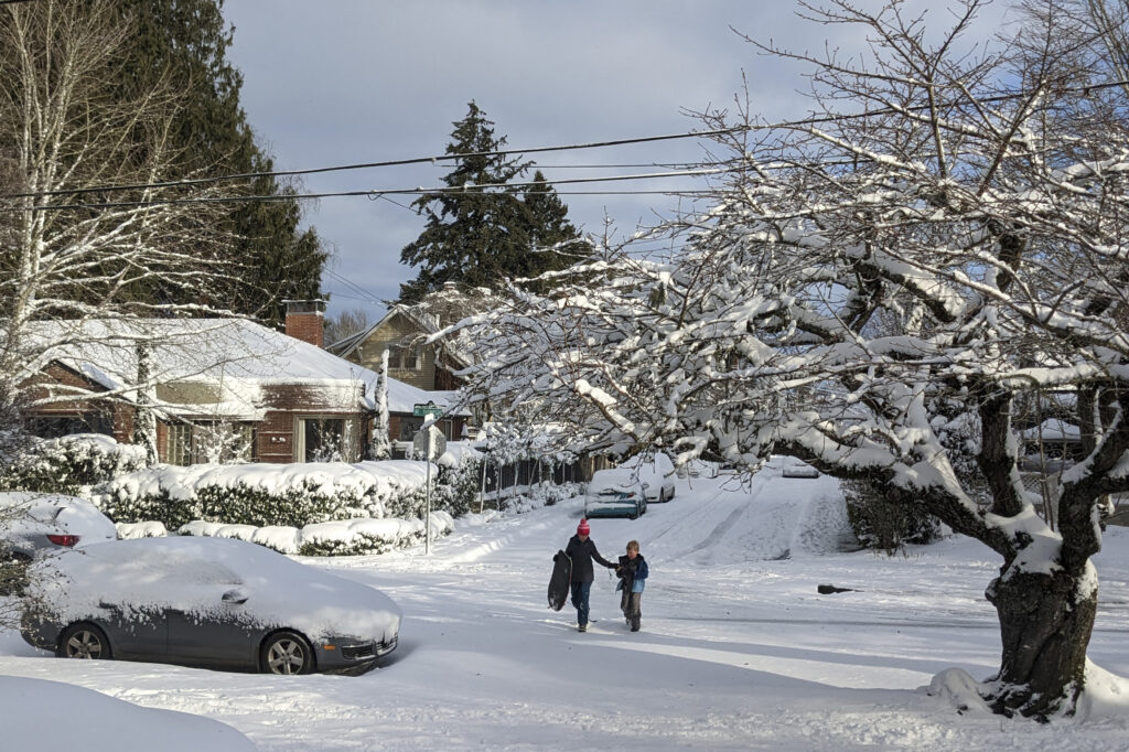 People make their way through a snow-covered street in the Grand Park neighborhood of Portland, Ore., Thursday Feb. 23, 2023. The city experienced its second snowiest day on record. (AP Photo/Drew Callister)
