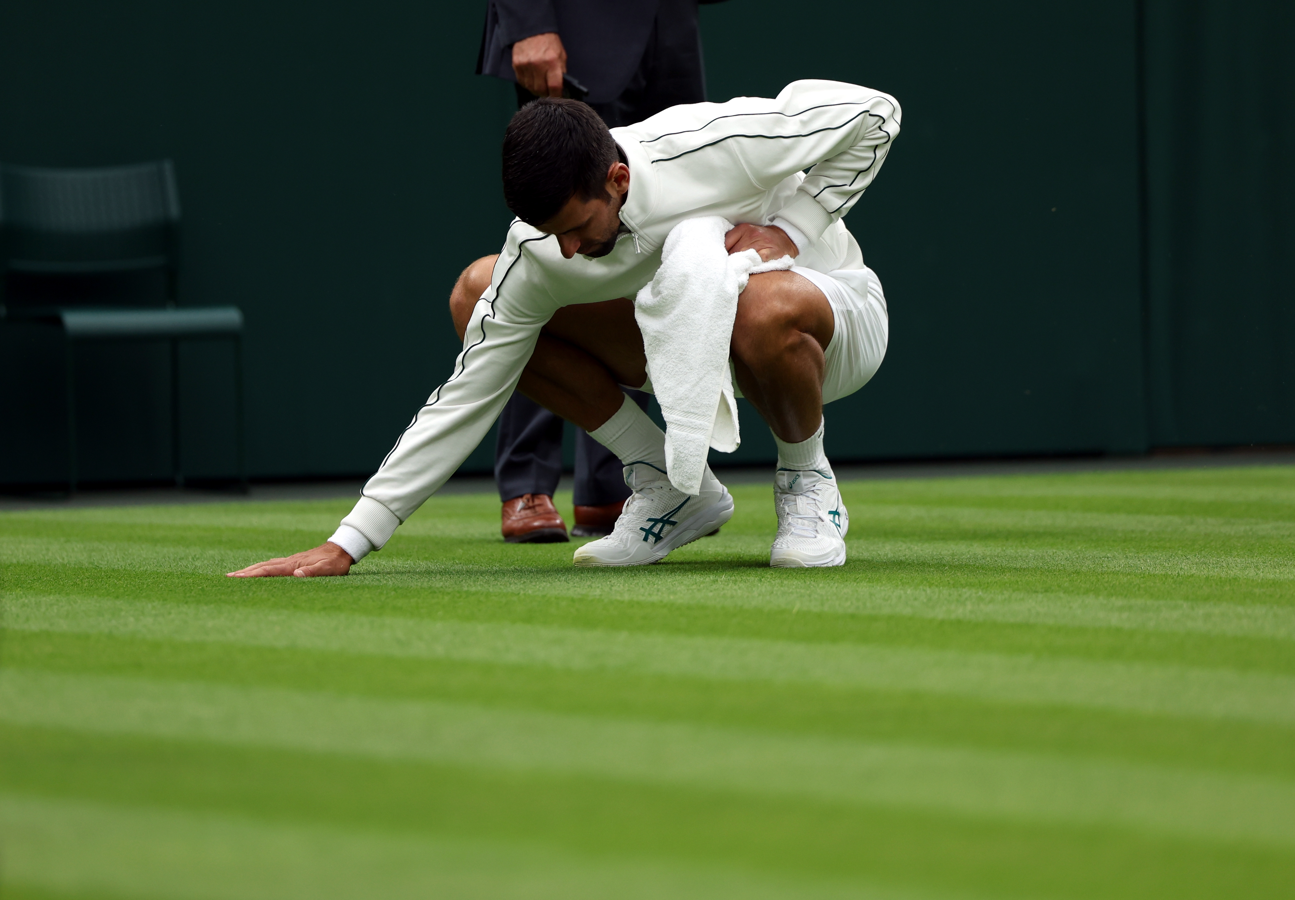 epa10724069 Novak Djokovic of Serbia checks the grass as his 1st round match against Pedro Cachin of Argentina was suspended due to rain at the Wimbledon Championships, Wimbledon, Britain, 03 July 2023.  EPA-EFE/NEIL HALL   EDITORIAL USE ONLY