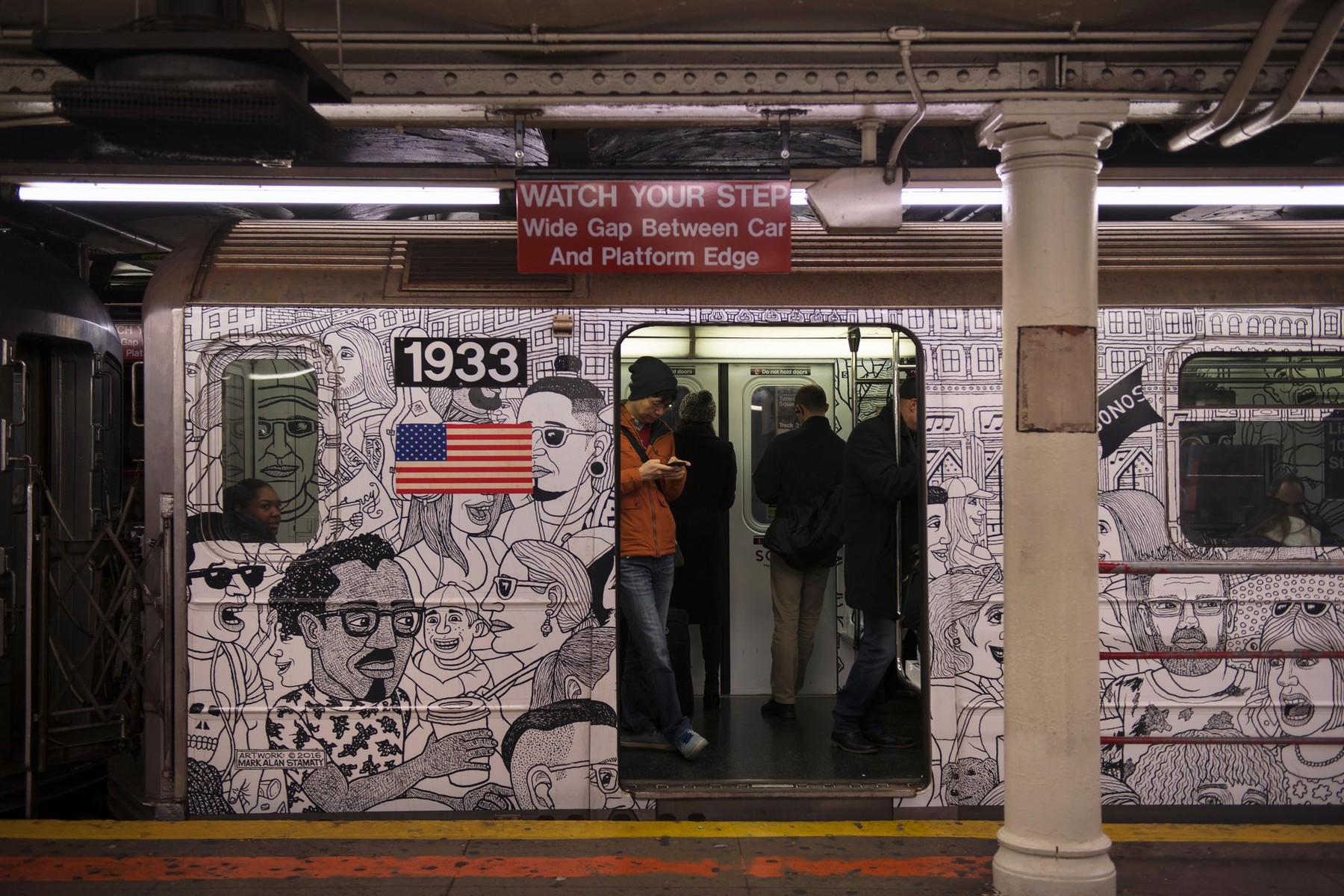 Passengers in a painted subway train during a stop at the waiting platform in a station. New York City, United States of America