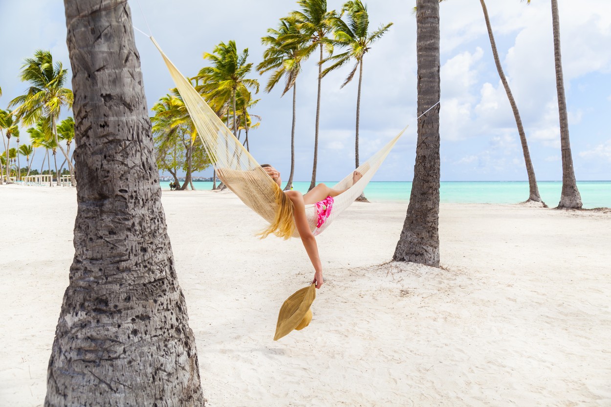 Young woman sunbathing in palm tree hammock at beach, Dominican Republic, The Caribbean
