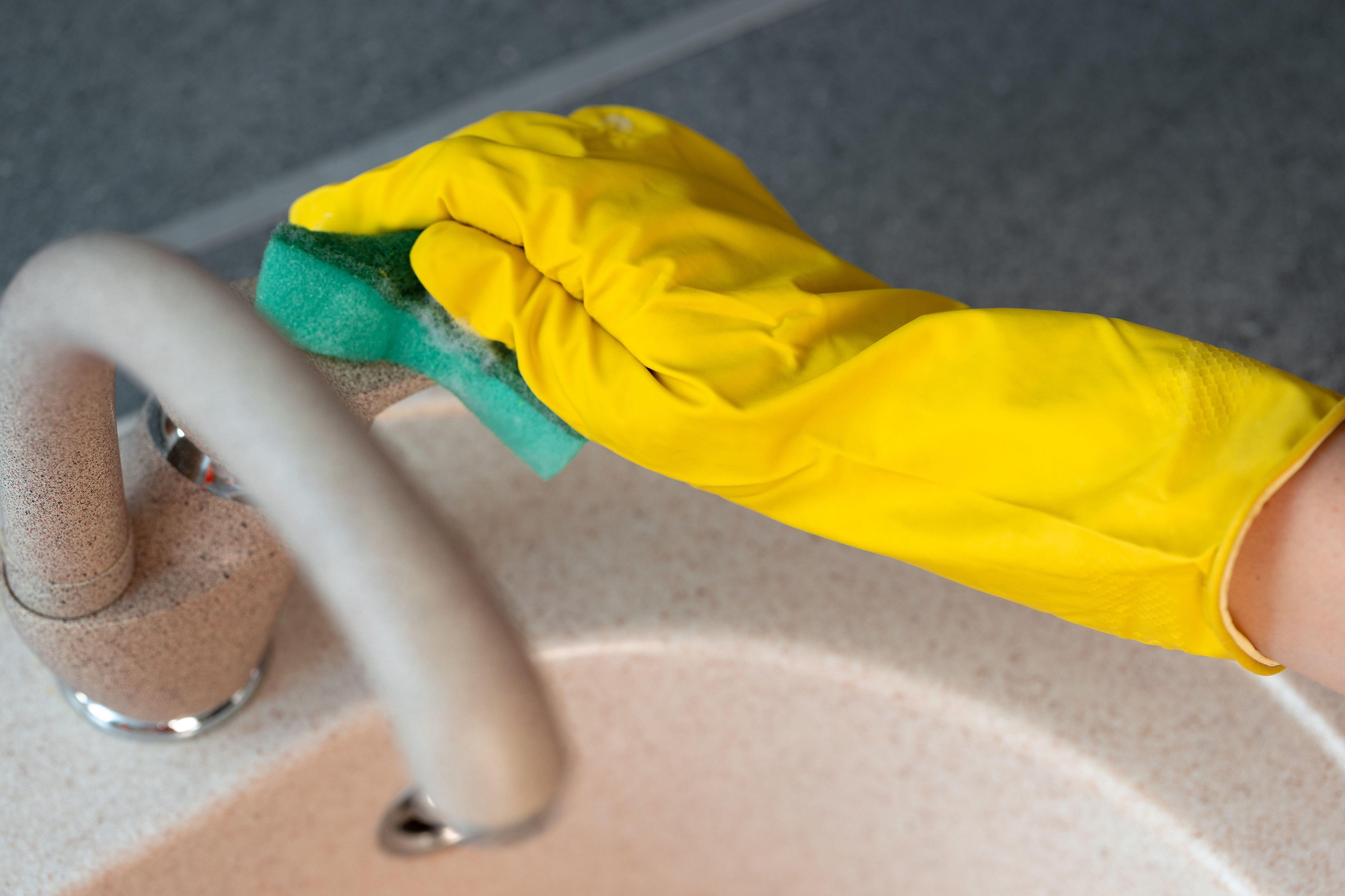 Hands in yellow gloves cleaning a sink with a sponge