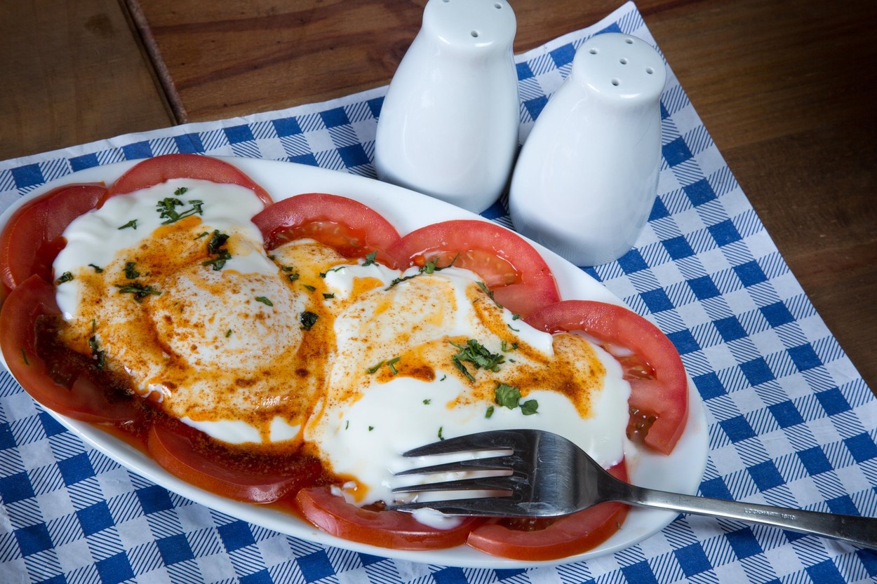 Traditional Turkish breakfast dish of Cilbir, poached egg, Garlic infused natural yoghurt topped with Paprika butter and served with sliced tomatoes