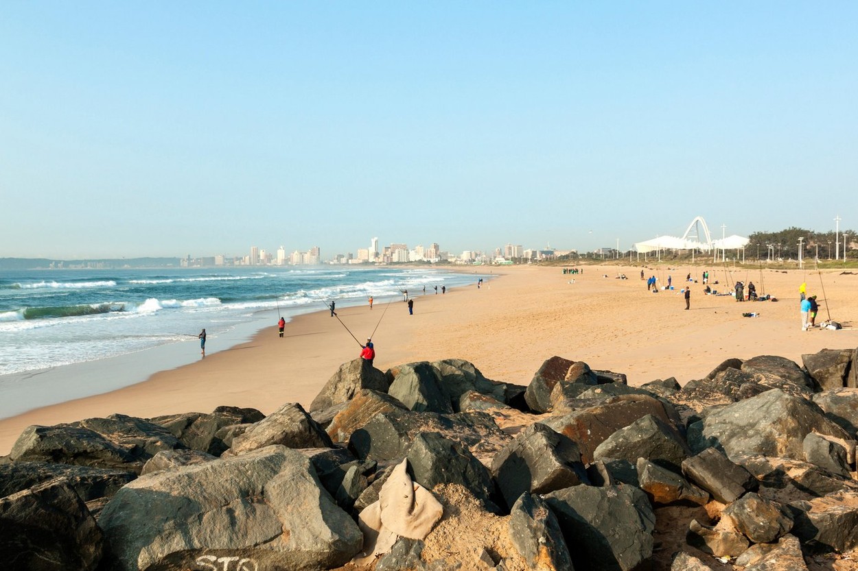 Many unknown fishermen on Blue Lagoon beach against Durban city skyline in South Africa