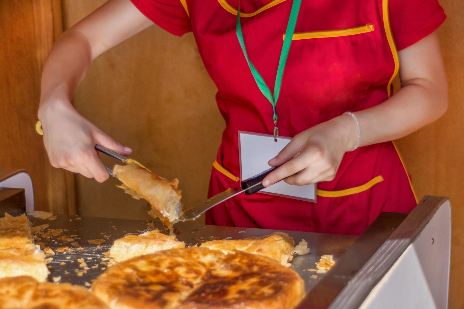 Young girl worker cuts a Balkan burek with cheese in bakery shop. Traditional pie breakfast in the Balkans concept. Close up, selective focus