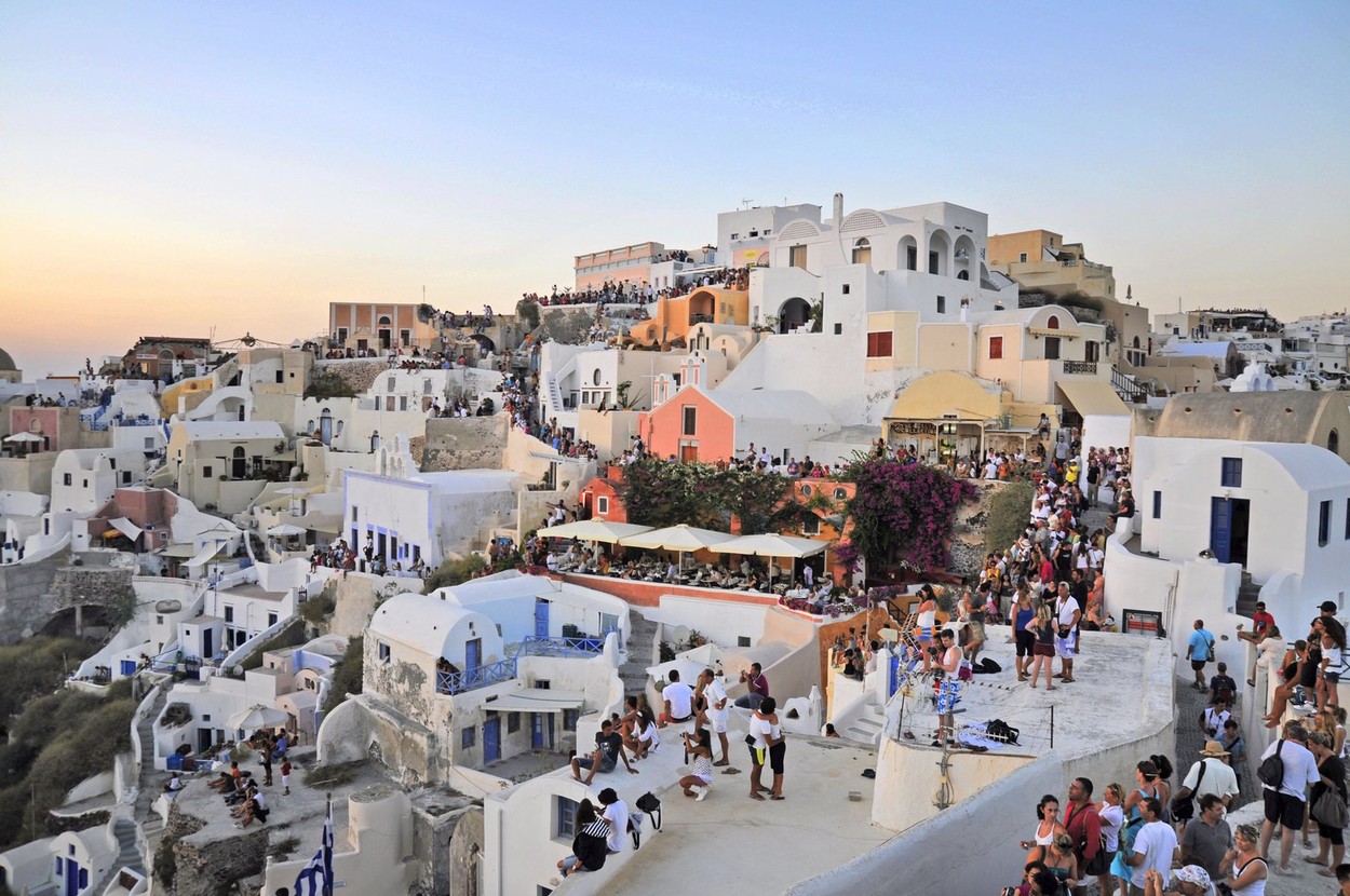 Tourists on roofs and streets of Oia watch Santorini sunset