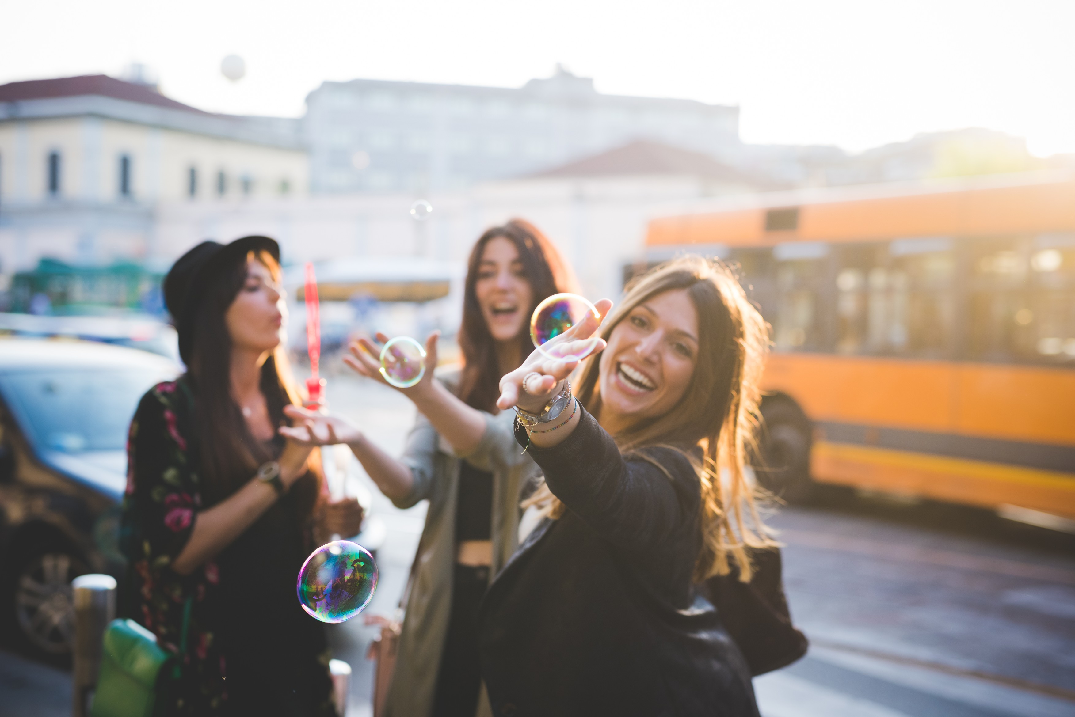 Three young female friends blowing bubbles on city street