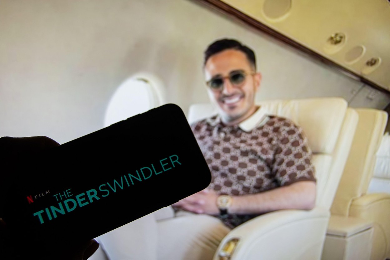 Rheinbach, Germany  24 February 2022,  The logo of the new Netflix Film "The Tinder Swindler" on the display of a smartphone in front of the TV