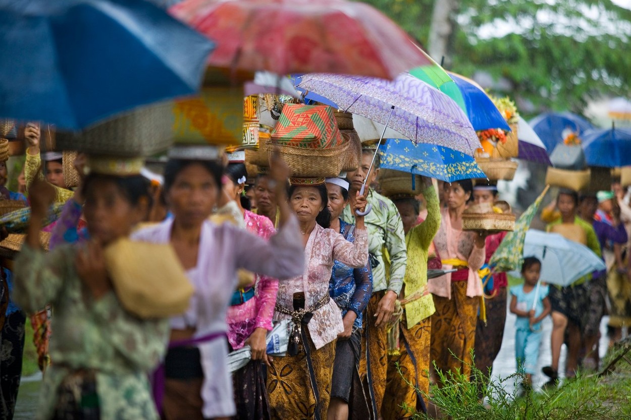 Procession of women carrying Hindu offerings in baskets on their heads during a tropical rain storm in Bali Indonesia