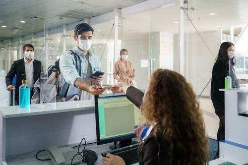 A male airline passengerwith mask is handing over his passport at the airline counter check in through an acrylic barrier for disease prevention coron