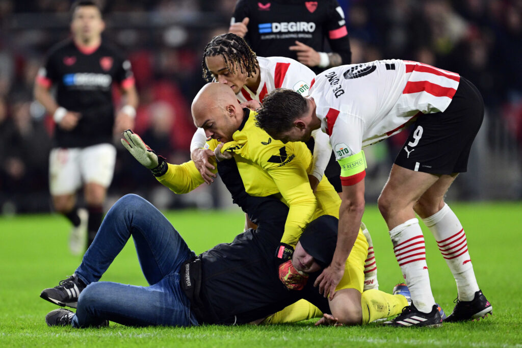 epa10486473 A pitch invader assaults Sevilla FC goalkeeper Marko Dmitrovic during the UEFA Europa league play-off soccer match between PSV Eindhoven and Sevilla FC, in Eindhoven, Netherlands, 23 February 2023.  EPA-EFE/OLAF KRAAK