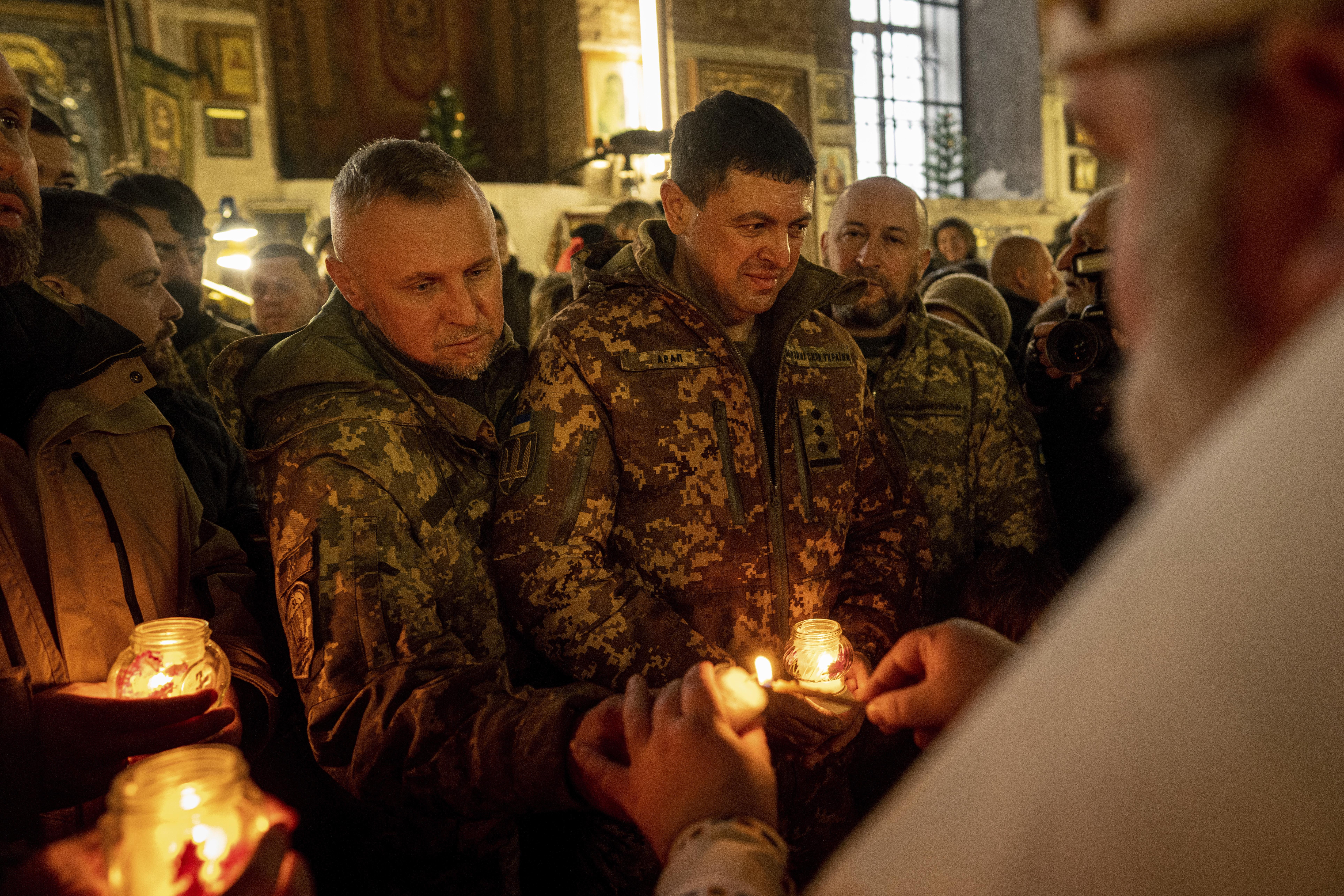 Ukrainian servicemen receive the Bethlehem Light of Peace from a priest during a Christmas church service in Kharkiv, Ukraine, Sunday, Dec. 25, 2022. (AP Photo/Evgeniy Maloletka)