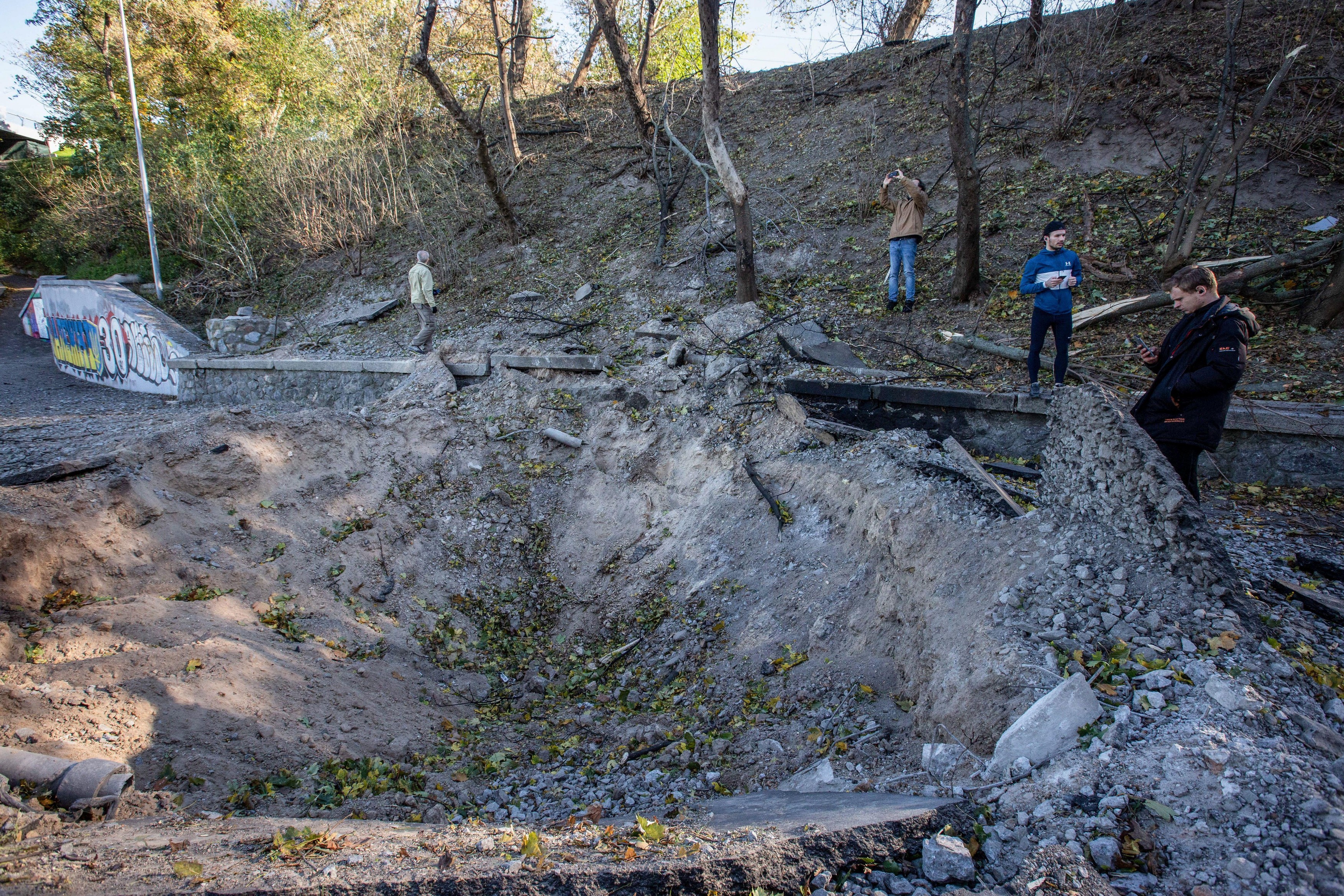 Kyiv, Ukraine. 10th Oct, 2022. People stand on the edge of a crater from a rocket explosion after a Russian missile attack in central Kyiv. Explosions have been reported in several districts of the Ukrainian capital Kyiv on October 10, 2022. At least 11 p