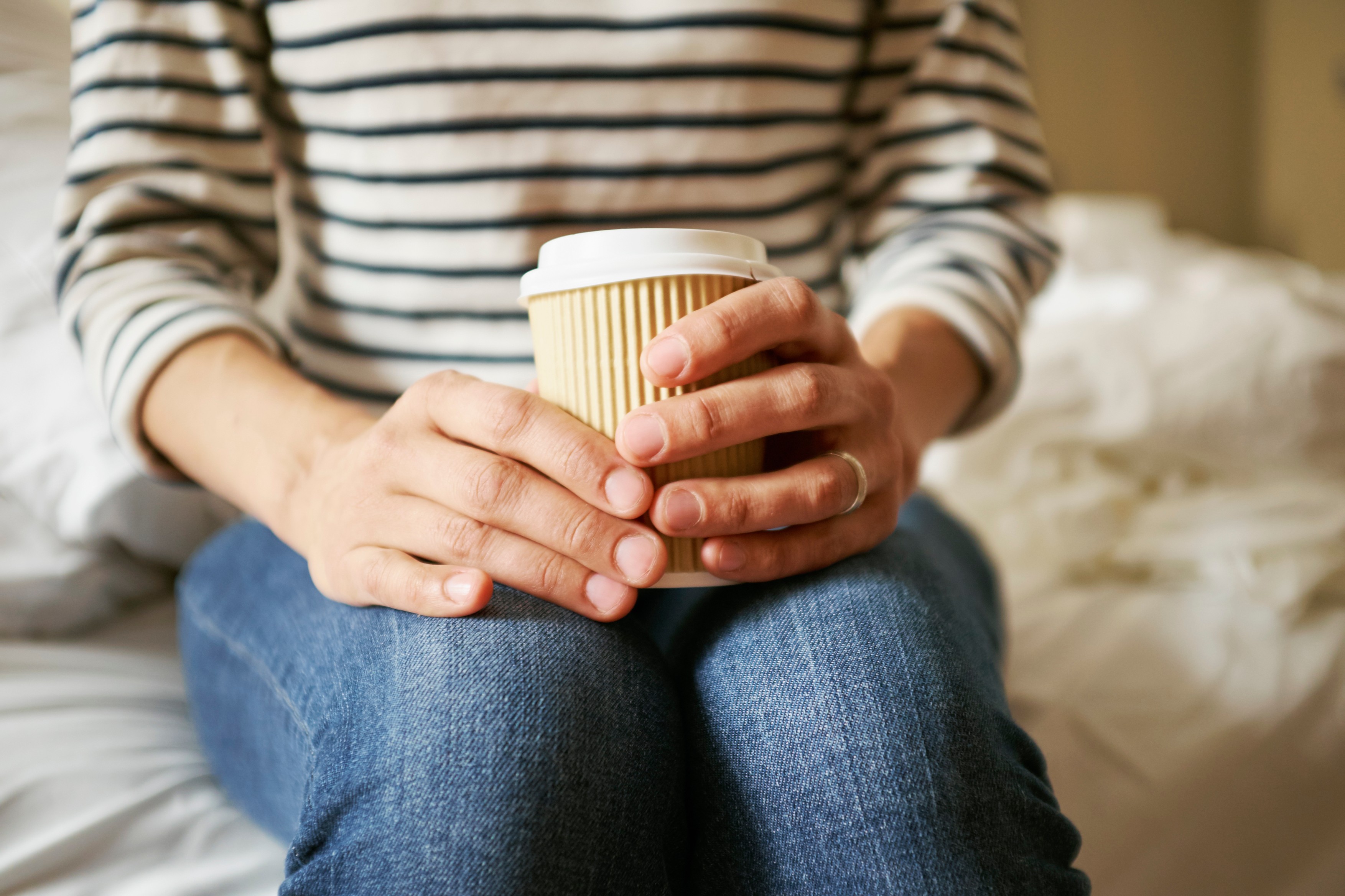 Womans hands holding takeaway coffee on bed