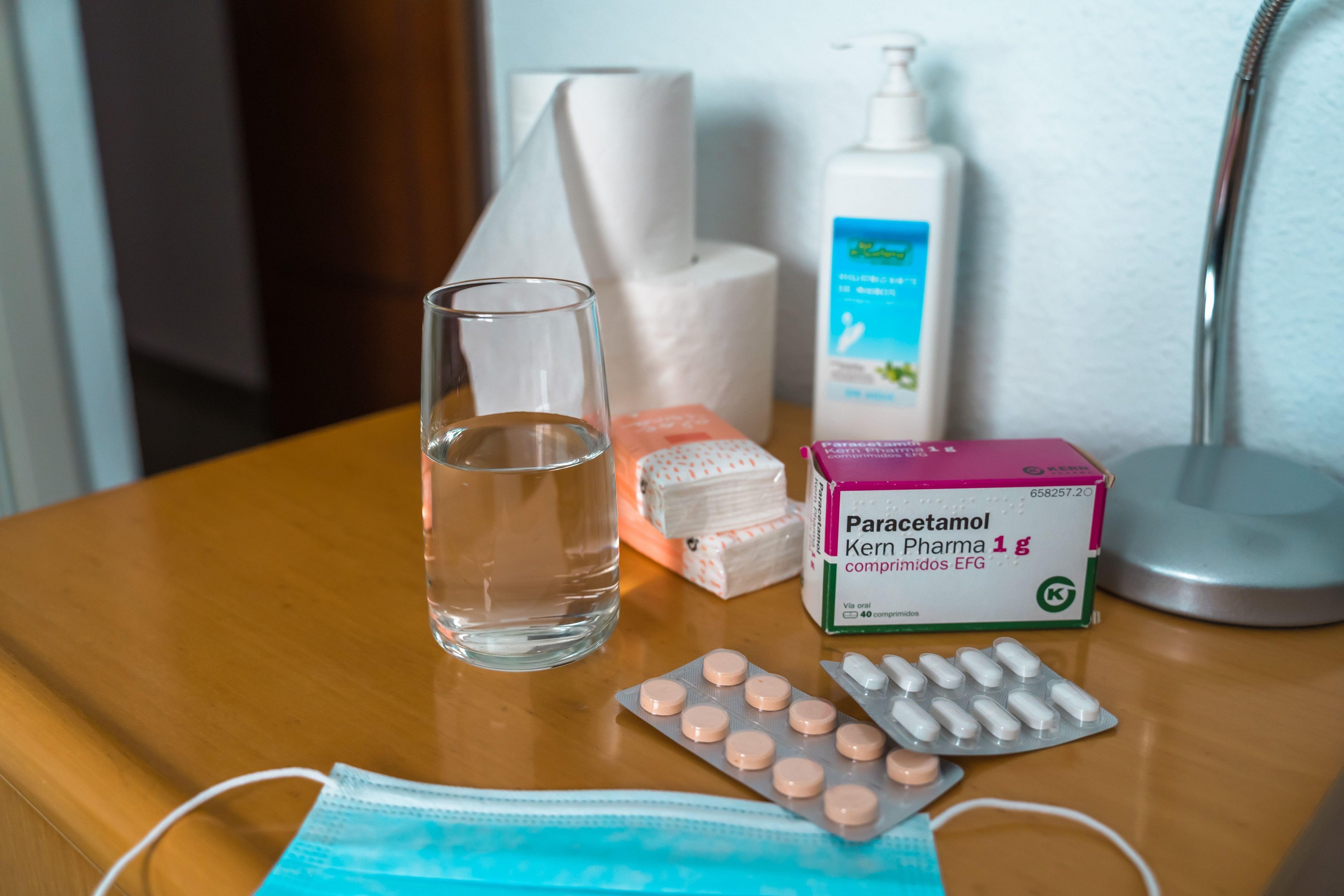 Paracetamol pills, glass of water, Sanitizing Gel, tissues and medical protection mask on the bedside table. Coronovirus COVID19 outbreak quarantine