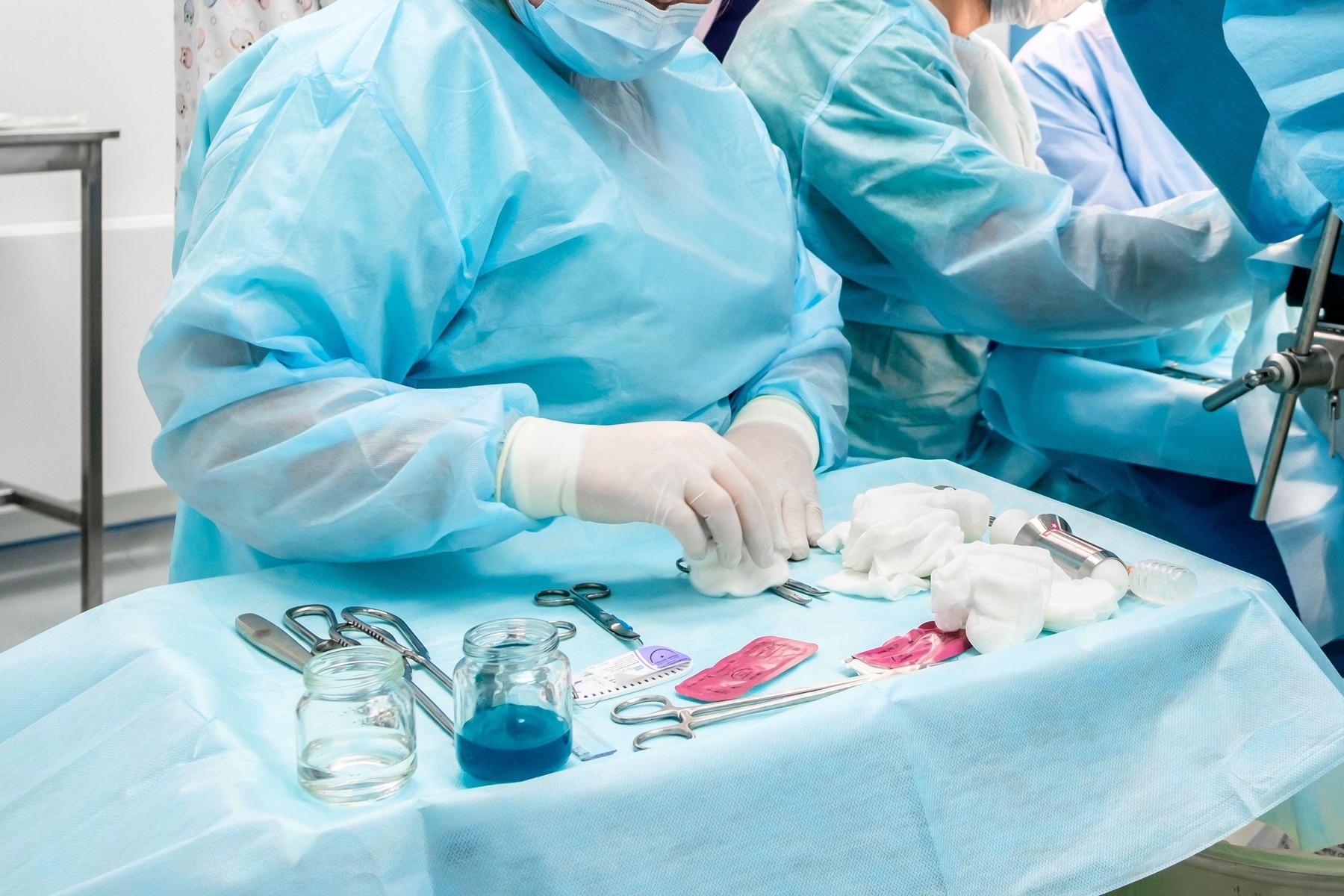 Sterile surgical instruments and glass containers with solutions on the table during a surgical operation. Above the table are the hands of a surgeon