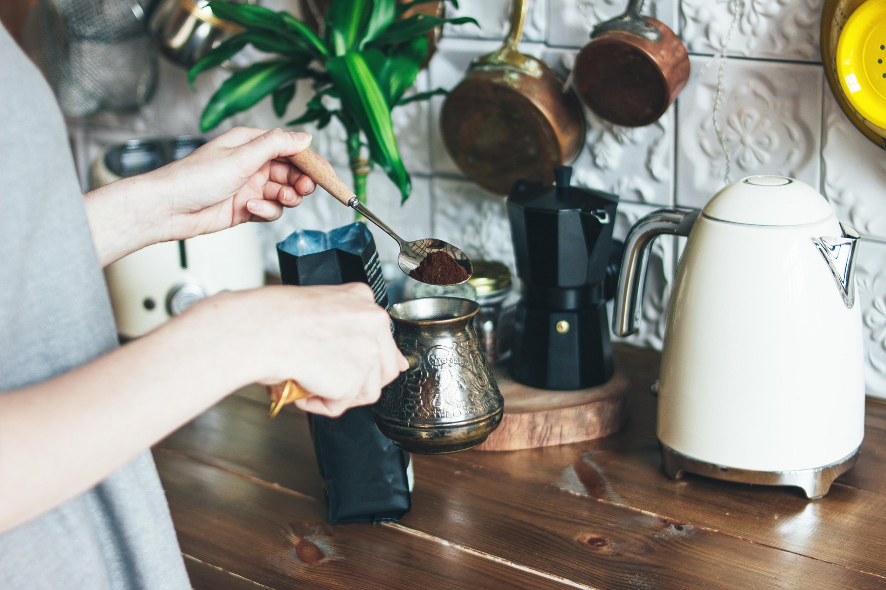 Young woman in grey dress making natural black coffee in pot in the kitchen, morning routine