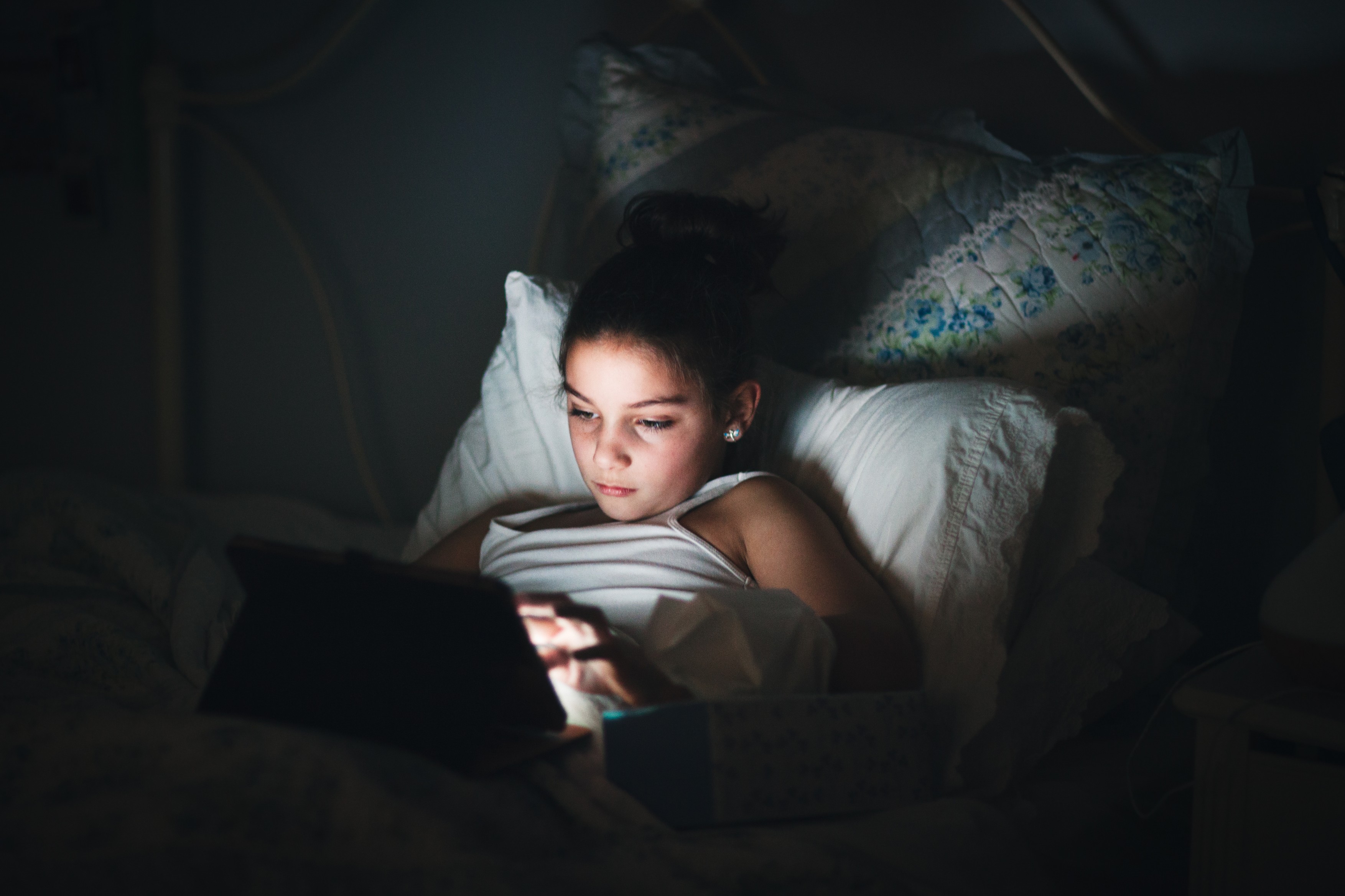 Girl in bed illuminated by light from digital tablet