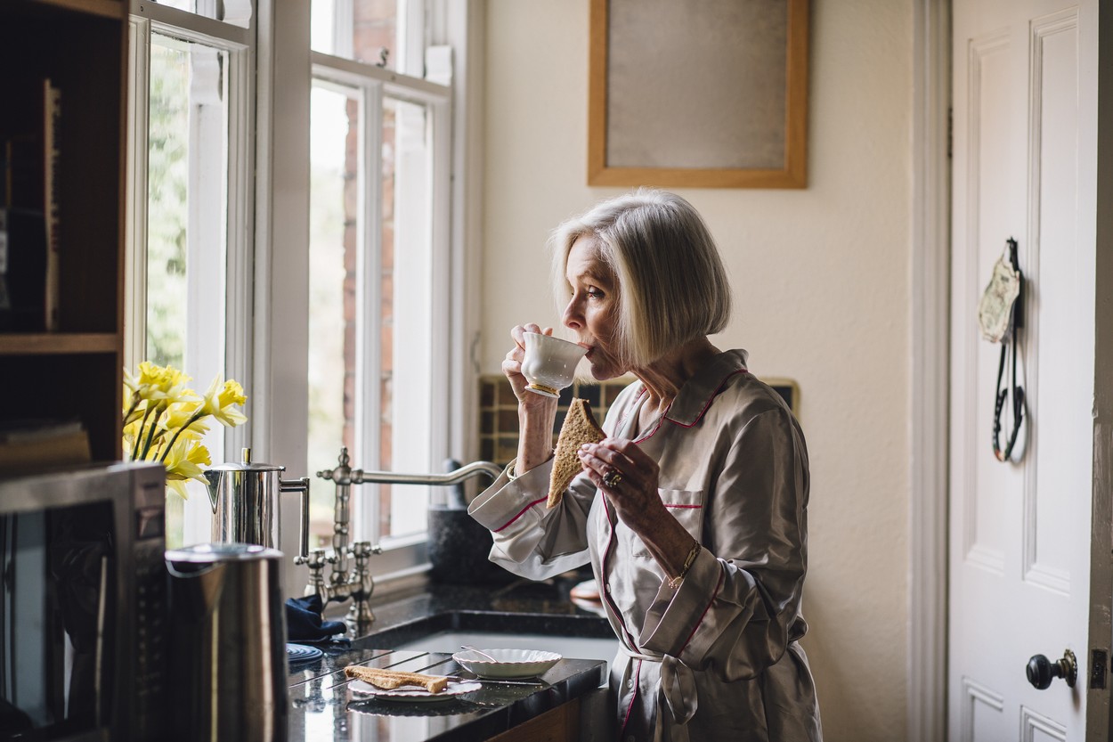 Senior woman is standing alone in her kitchen in her dressing gown,  eating toast and dirnking tea.,Image: 337856573, License: Royalty-free, Restrictions: , Model Release: yes, Credit line: Graham Oliver / Panthermedia / Profimedia