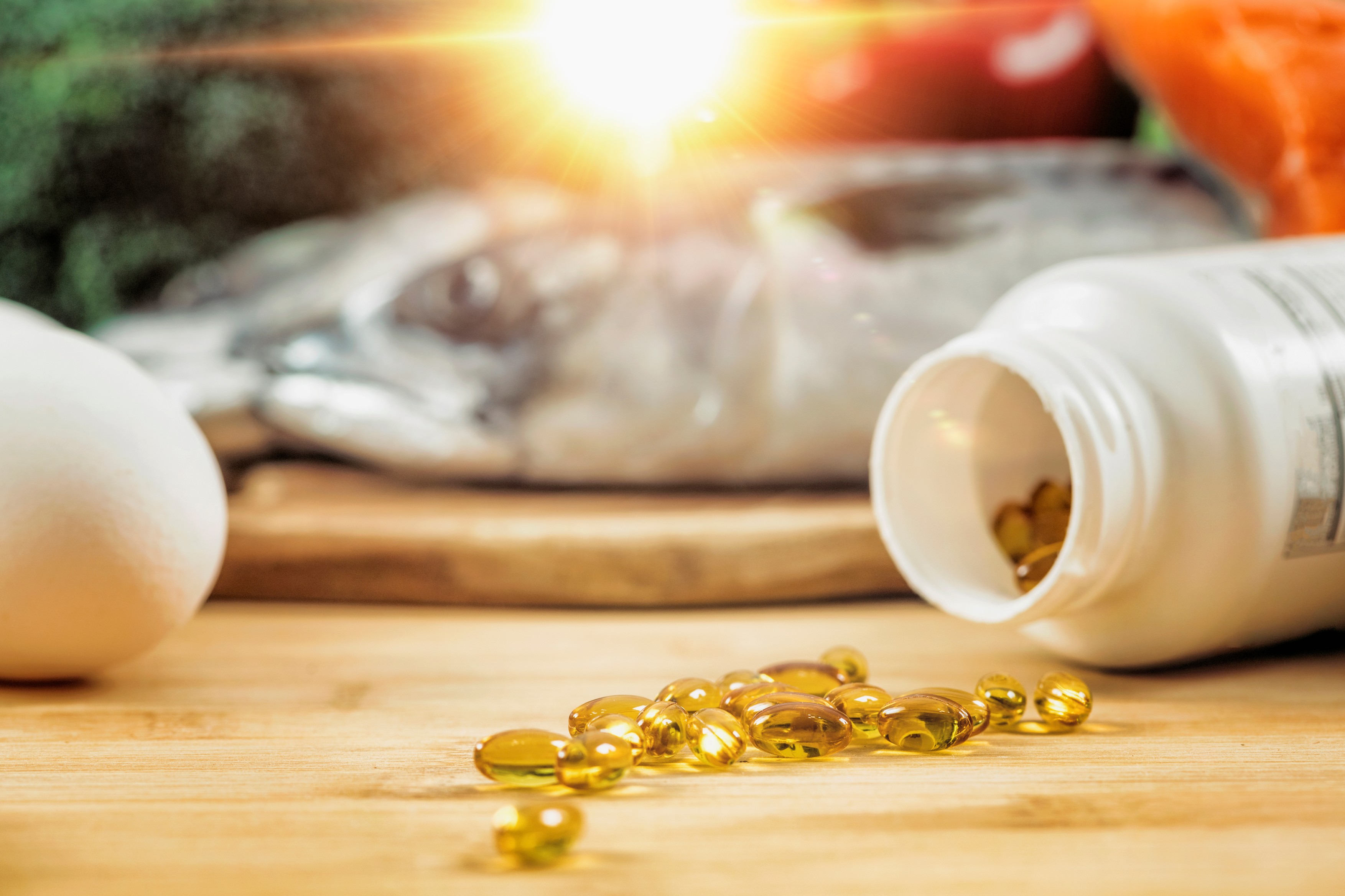 Supplement bottle with gel capsules on a wooden table. Natural food sources of vitamin D in background.,Image: 443197132, License: Royalty-free, Restrictions: , Model Release: no, Credit line: MICROGEN IMAGES / Sciencephoto / Profimedia