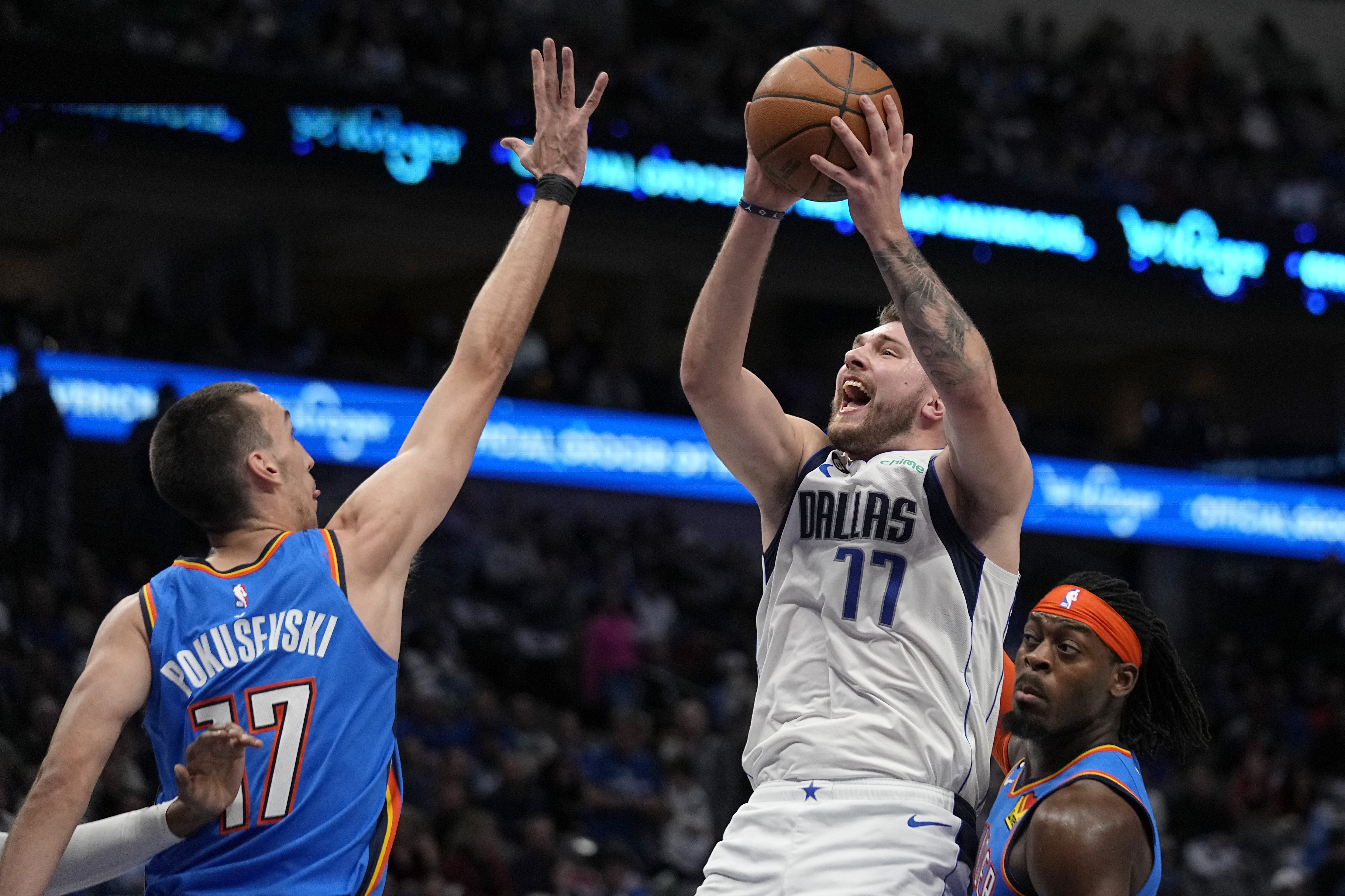 Dallas Mavericks guard Luka Doncic (77) shoots as Oklahoma City Thunder's Aleksej Pokusevski (17) and Luguentz Dort, right, defend in the first half of an NBA basketball game, Monday, Dec. 12, 2022, in Dallas. (AP Photo/Tony Gutierrez)