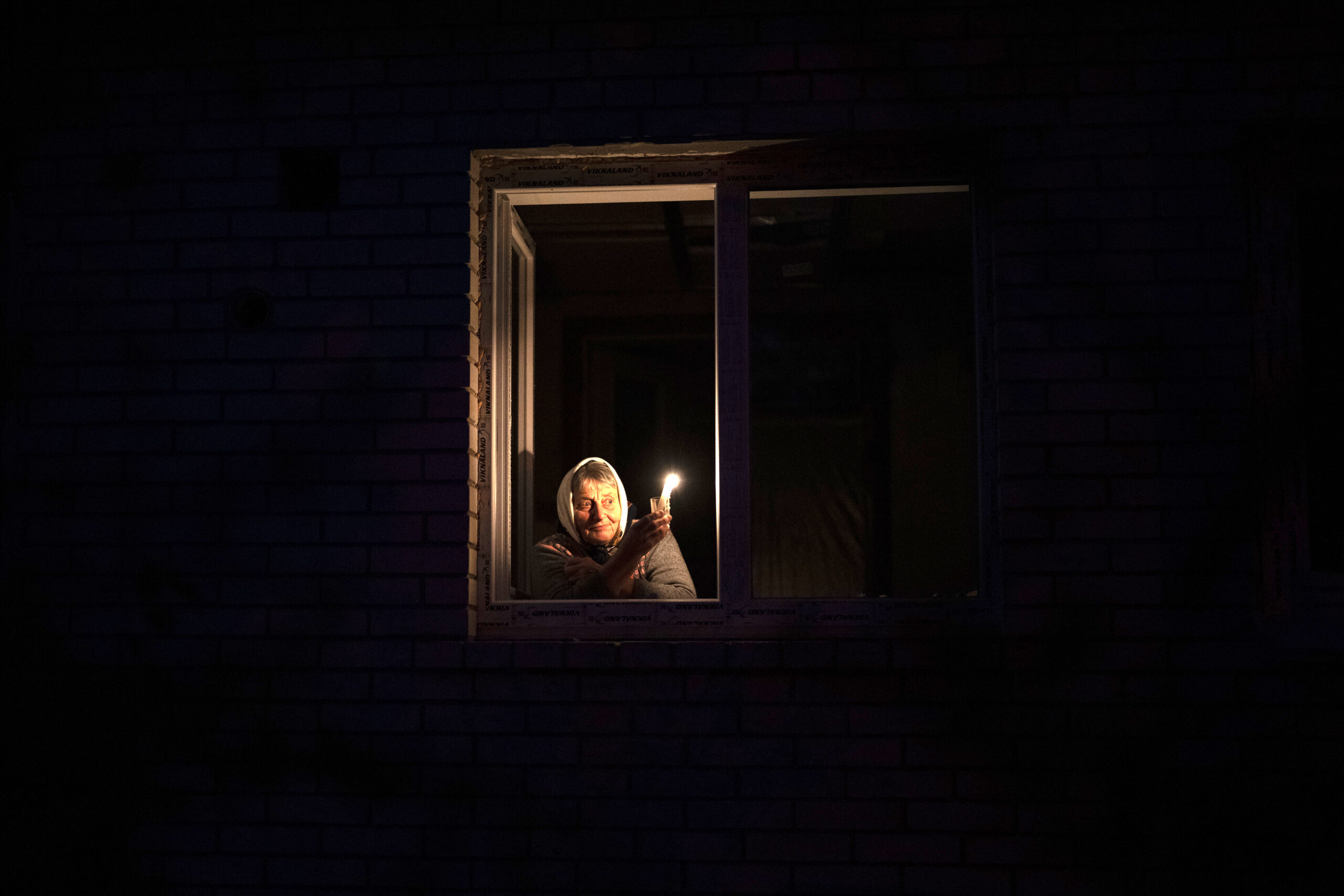 Catherine, 70, looks out the window while holding a candle for light inside her house during a power outage, in Borodyanka, Kyiv region, Ukraine, Thursday, Oct. 20, 2022. (AP Photo/Emilio Morenatti)